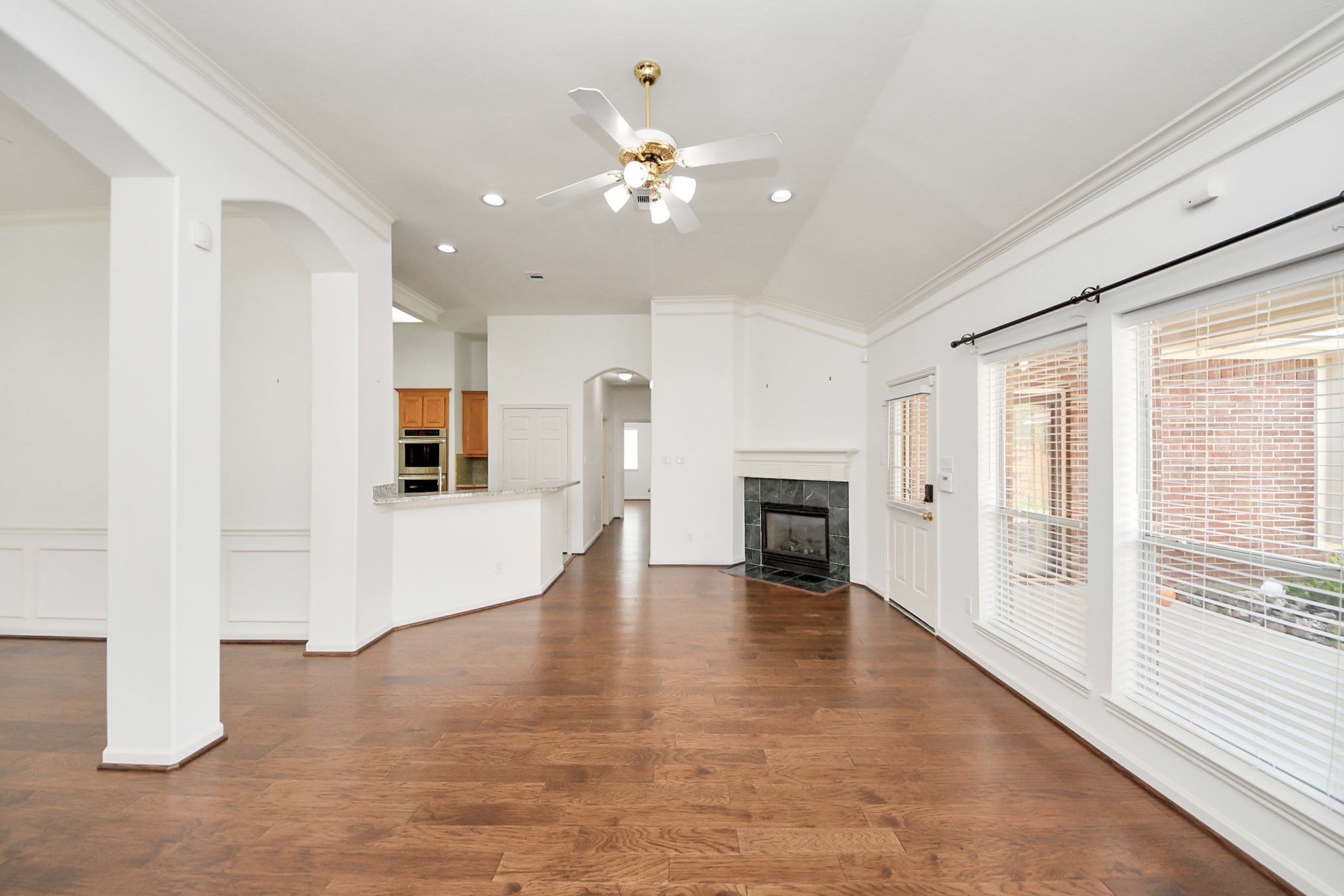 Spacious bedroom area featuring elegant hardwood floors, a cozy fireplace, and abundant natural light through large windows, seamlessly connecting to a modern kitchen with an inviting breakfast bar.