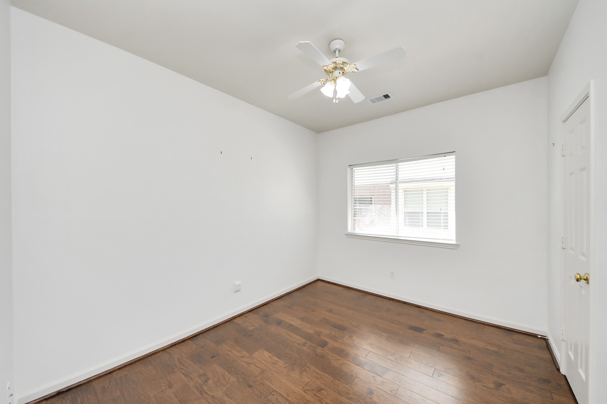 Bright bedroom featuring hardwood floors, a ceiling fan, and a large window for natural light.