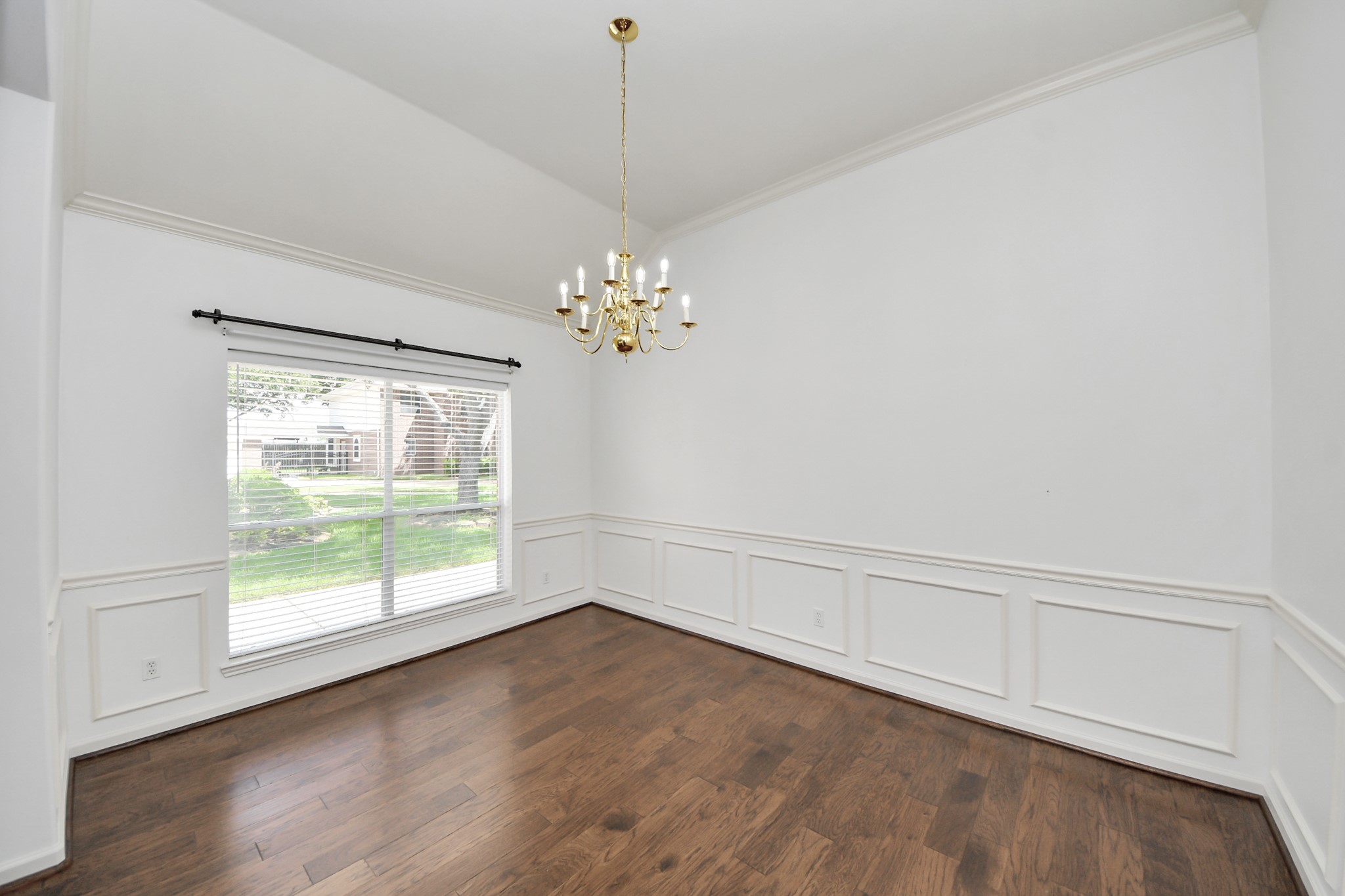 Elegant dining room featuring rich hardwood floors, a classic chandelier, and a large window offering abundant natural light.