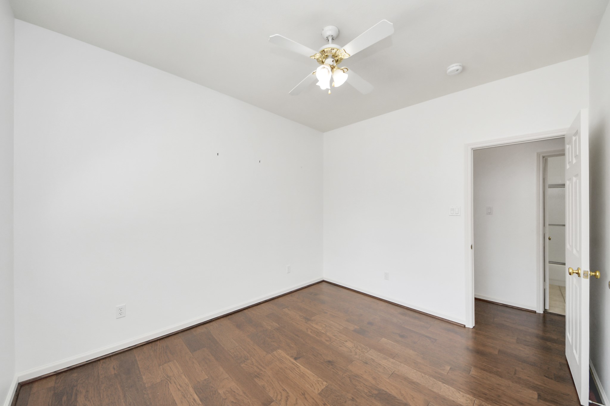 Bright and airy room with rich hardwood floors and a ceiling fan, offering a blank canvas ready for your personal touch.