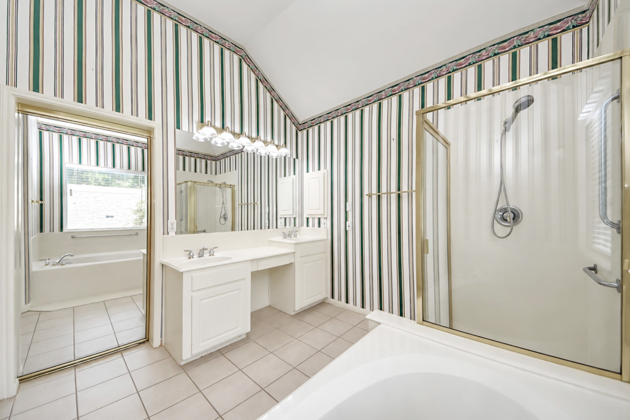 Spacious bathroom featuring a dual vanity, separate shower, and a relaxing bathtub, all accented by classic striped wallpaper and ample natural light.