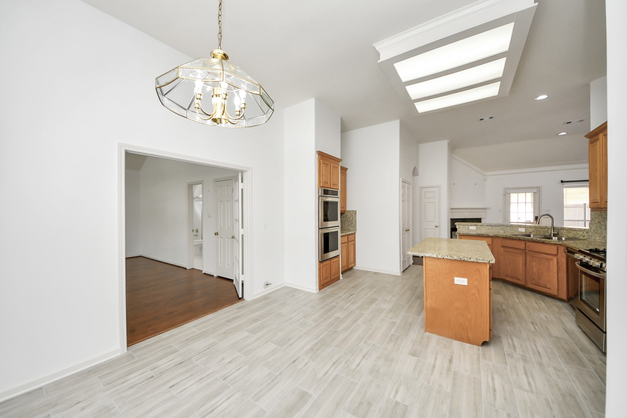 Spacious kitchen with granite countertops, modern appliances, and ample cabinetry, flowing seamlessly into a bright dining area under a stylish chandelier.