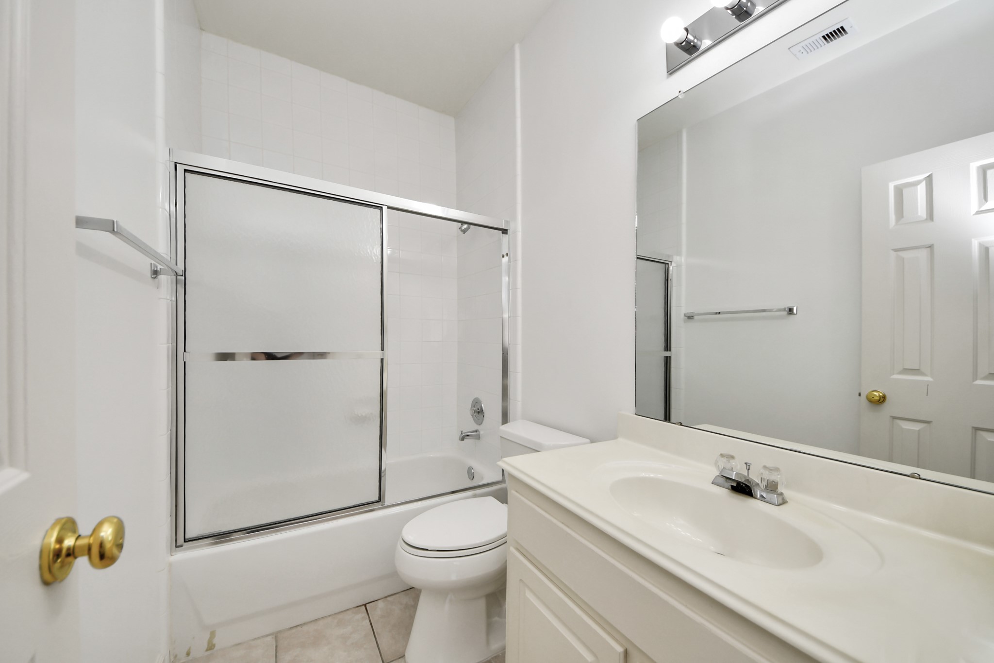 Bright and clean bathroom featuring a sleek vanity, large mirror, and a shower-tub combo with sliding glass doors.