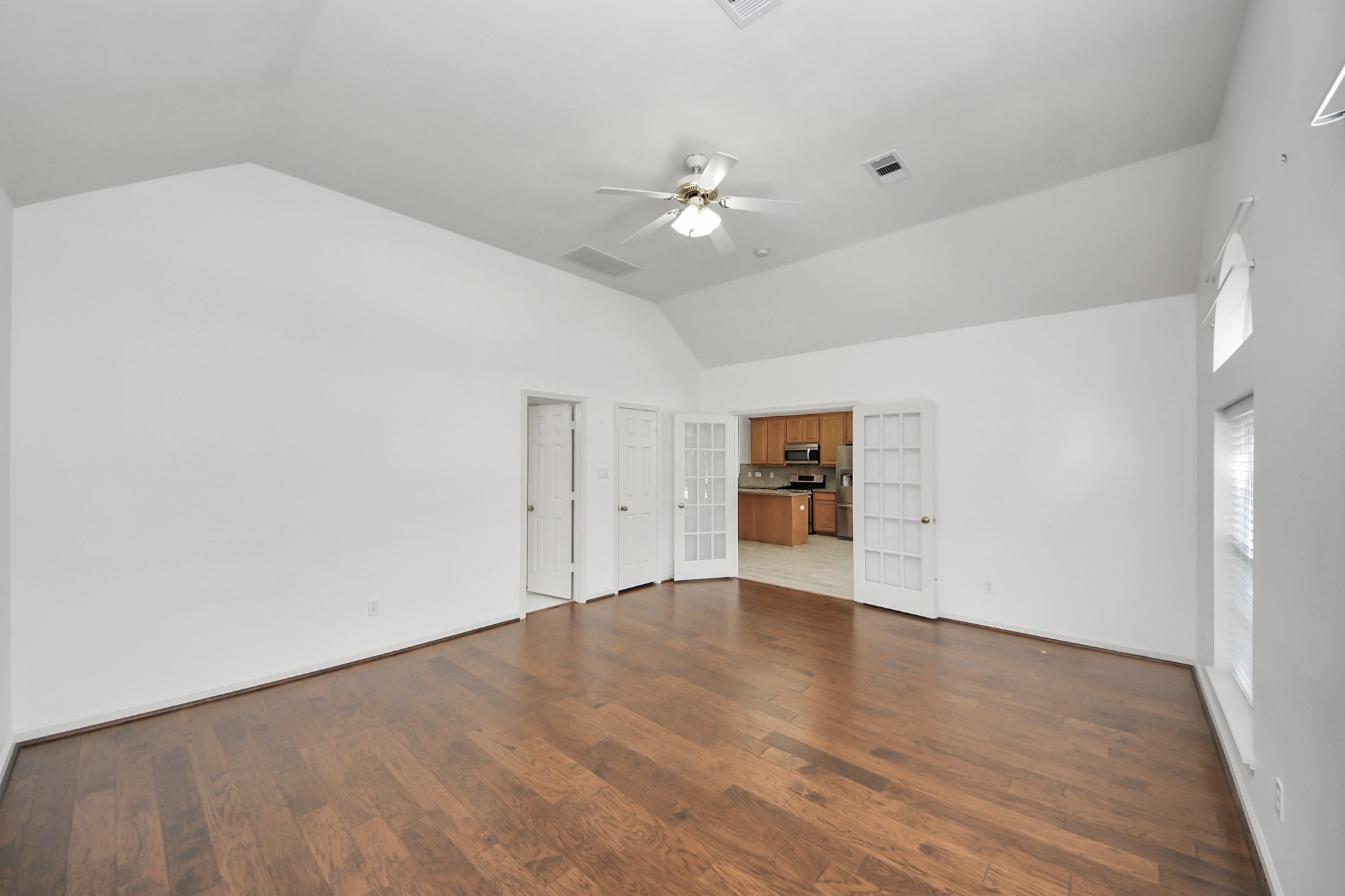 Spacious living area featuring elegant hardwood floors and high ceilings, with French doors opening to a modern kitchen.