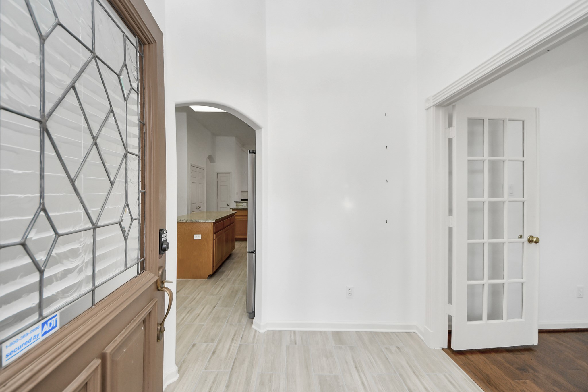 Inviting entryway with a decorative glass front door, leading to a bright interior featuring elegant French doors and a glimpse of the spacious kitchen with warm wood cabinetry and granite countertops.