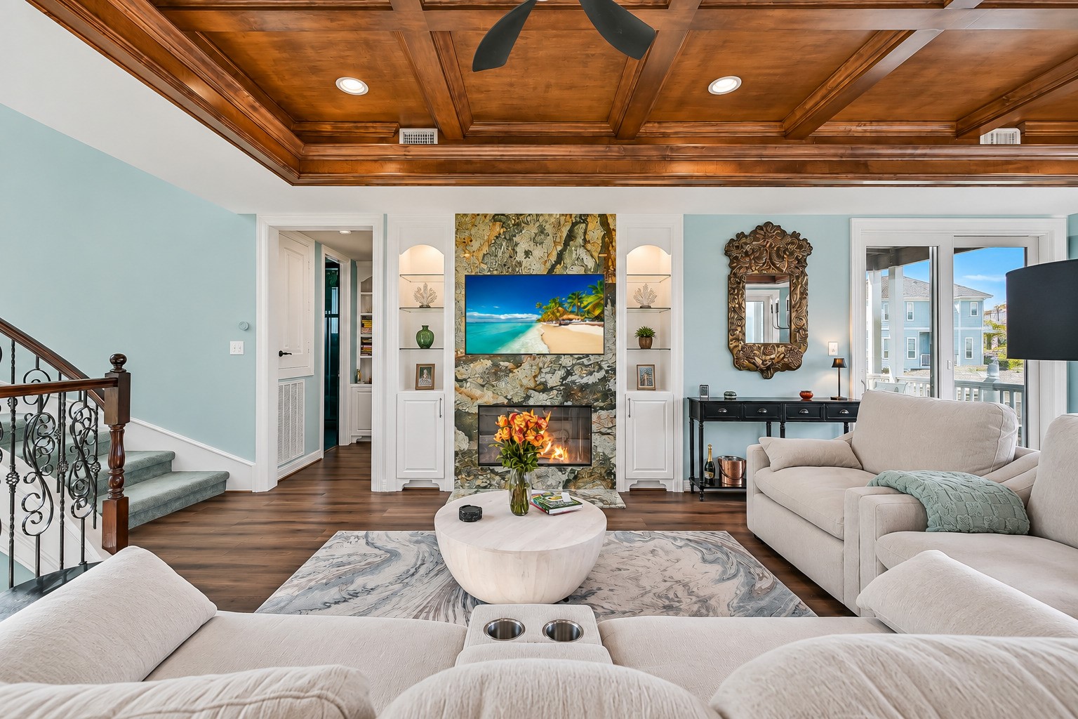 A Brazilian granite gas fireplace anchors one end of the room while floor-to-ceiling windows flood the space with natural light and frame the water beyond. Beautiful luxury waterproof wide-plank flooring, designer paint, and custom built-in cabinetry make this a living room that feels as intentional as it is beautiful.