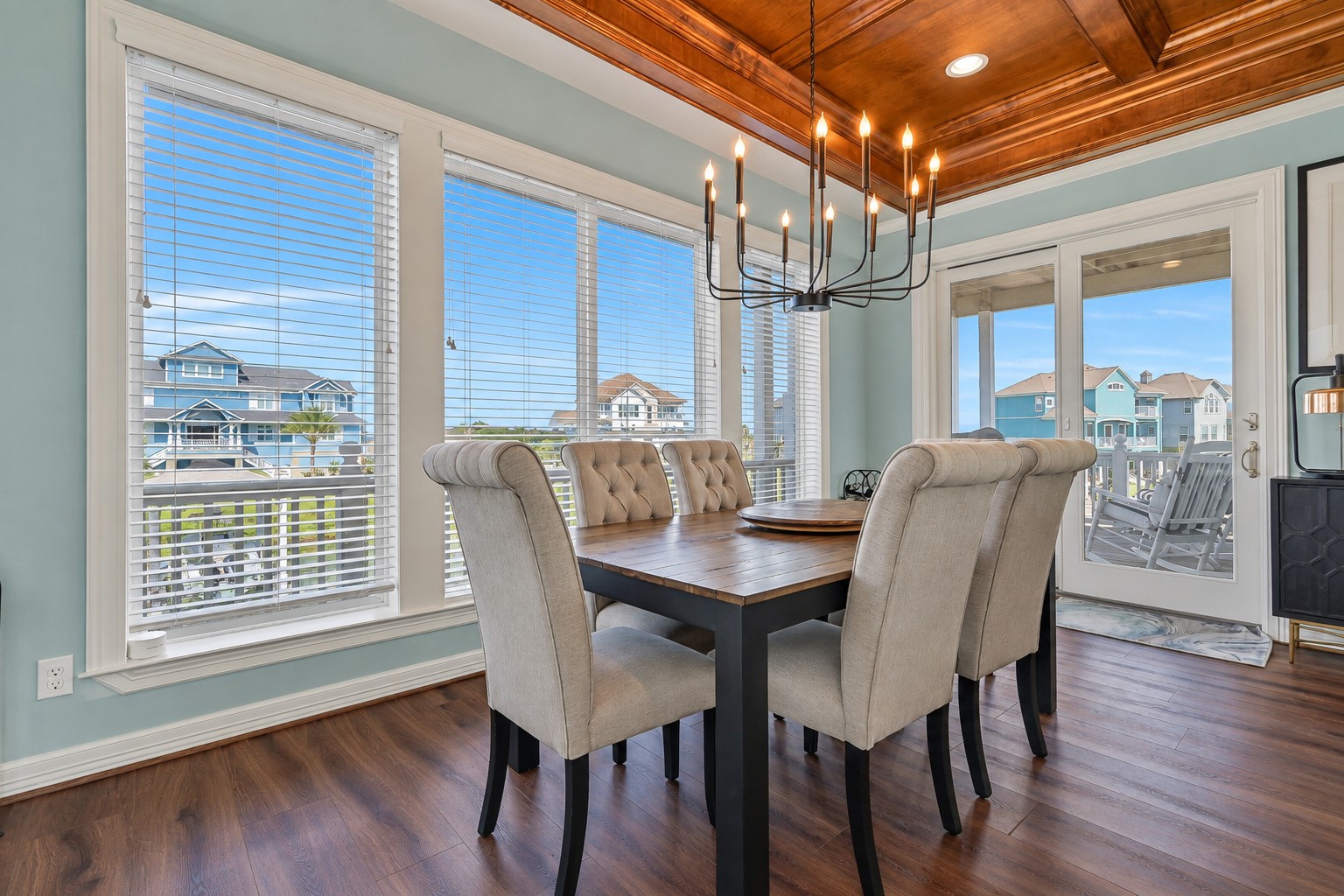 Dinner with a water view. The open-concept dining area sits at the heart of the main living floor, flowing seamlessly between the chef's kitchen and the connecting balconies beyond. Natural light pours in from every angle, and the hand-crafted coffered ceiling overhead makes every meal feel like an occasion.