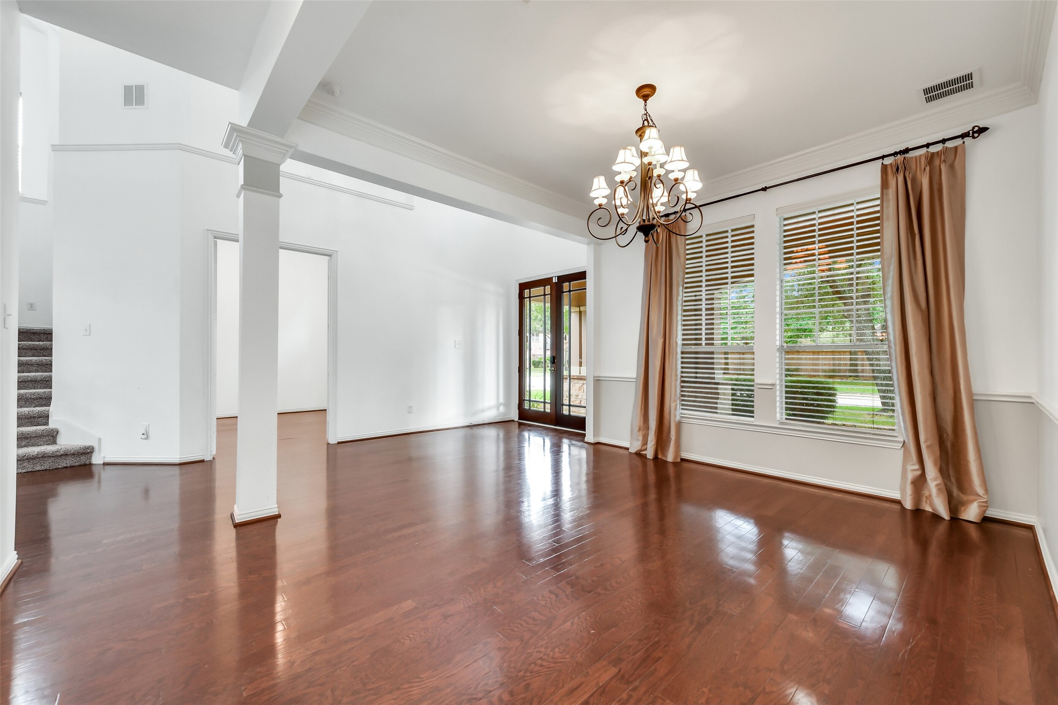 This view of the formal dining room highlights designer chandelier, custom drapery, and window blinds, with open doors leading seamlessly into the first-floor office
