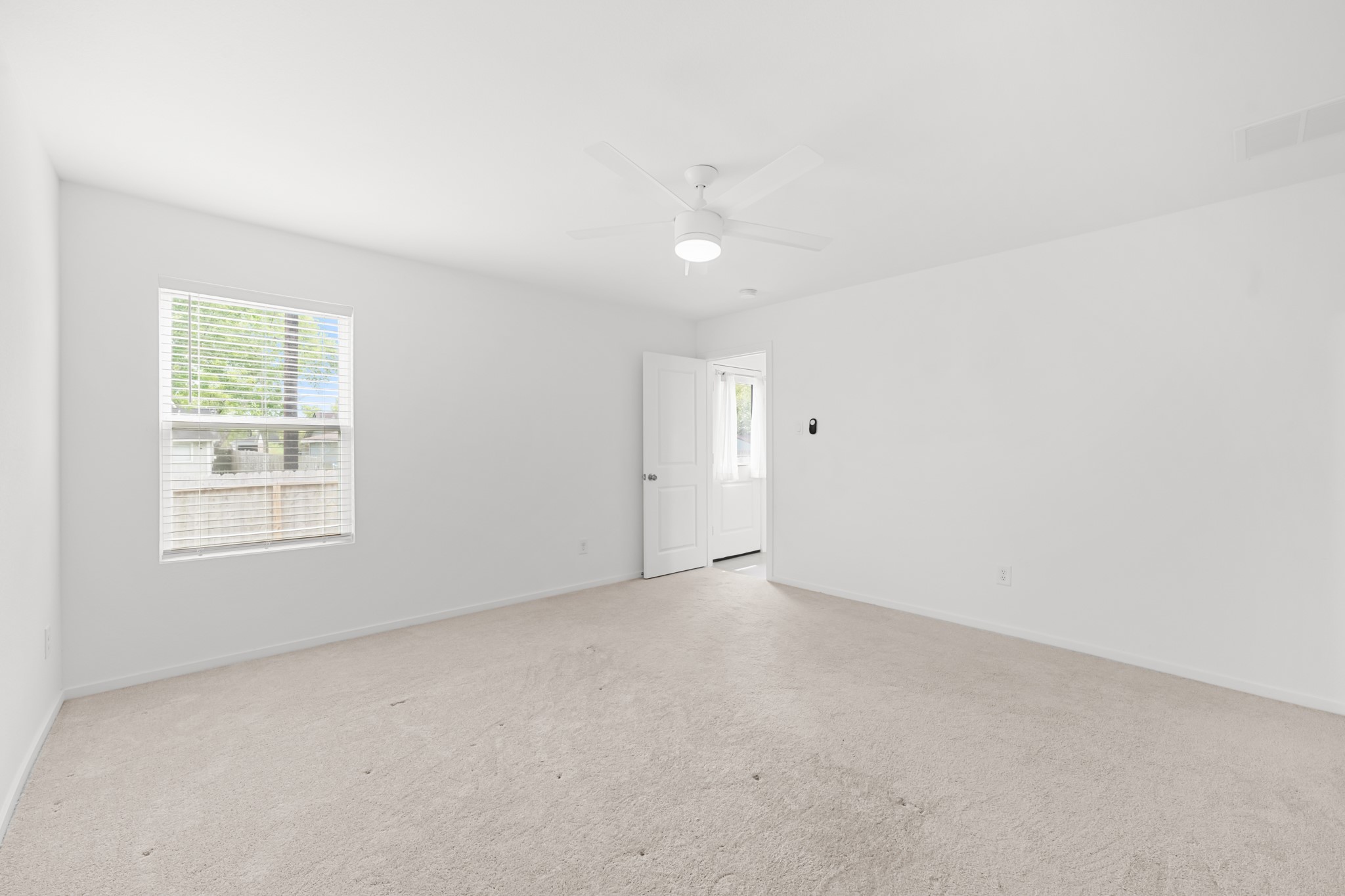 Spacious primary bedroom features neutral carpeting, a ceiling fan, and a large window that brings natural light into the room.