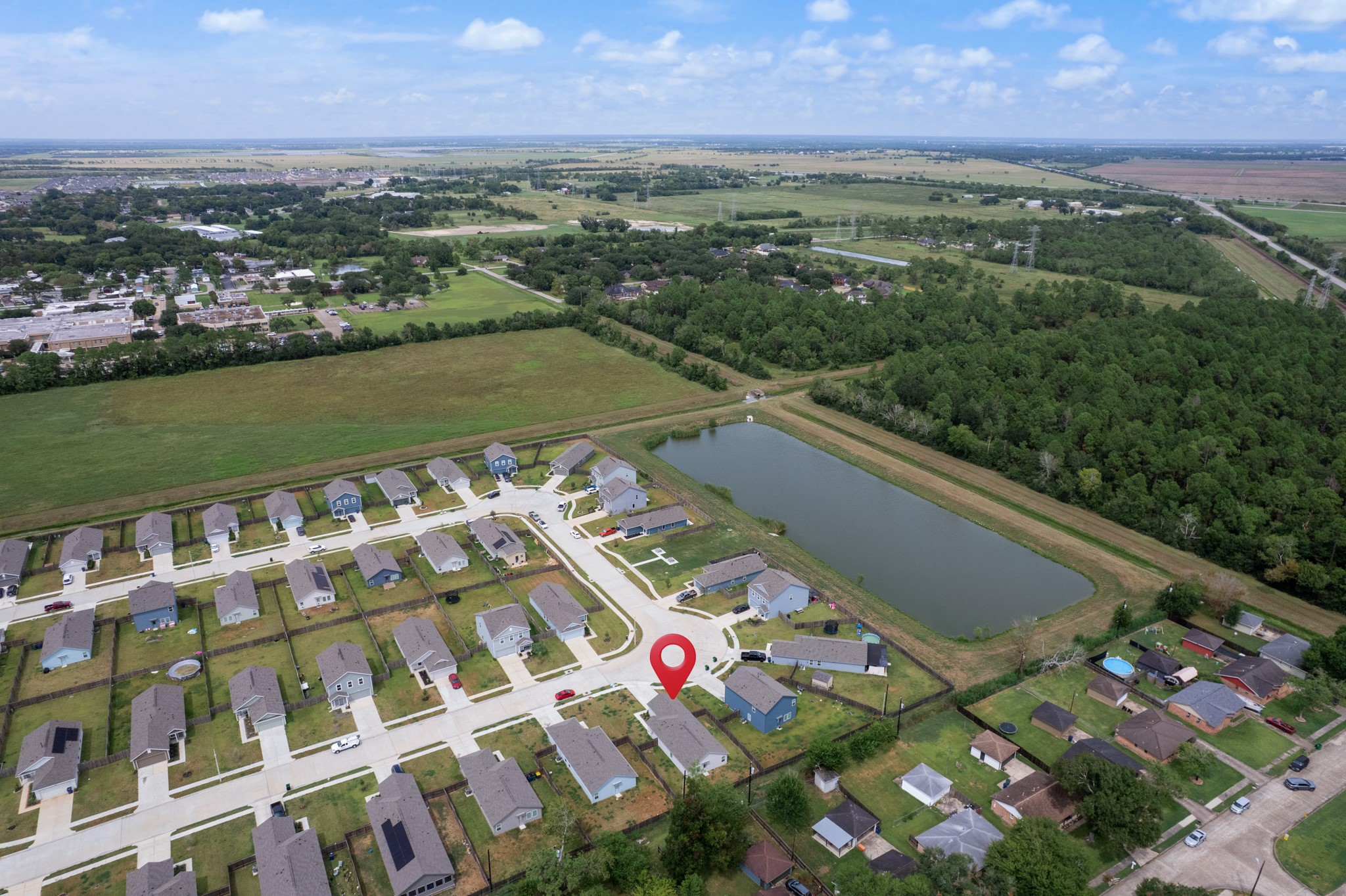 Wide aerial view showcases the neighborhood layout, nearby pond, and surrounding green space, with the property clearly marked.
