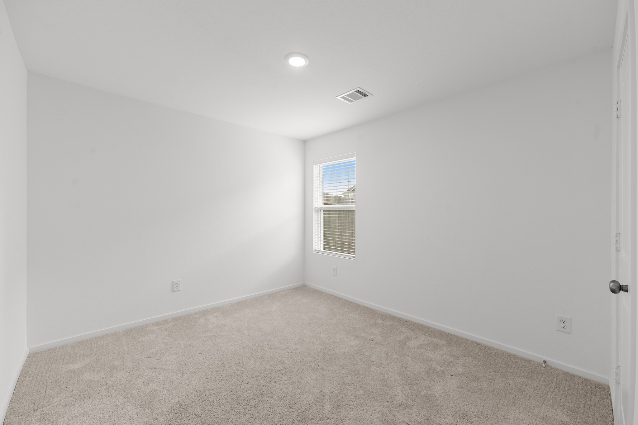 Secondary bedroom offers neutral finishes, soft carpeting, recessed lighting, and a window providing natural light.