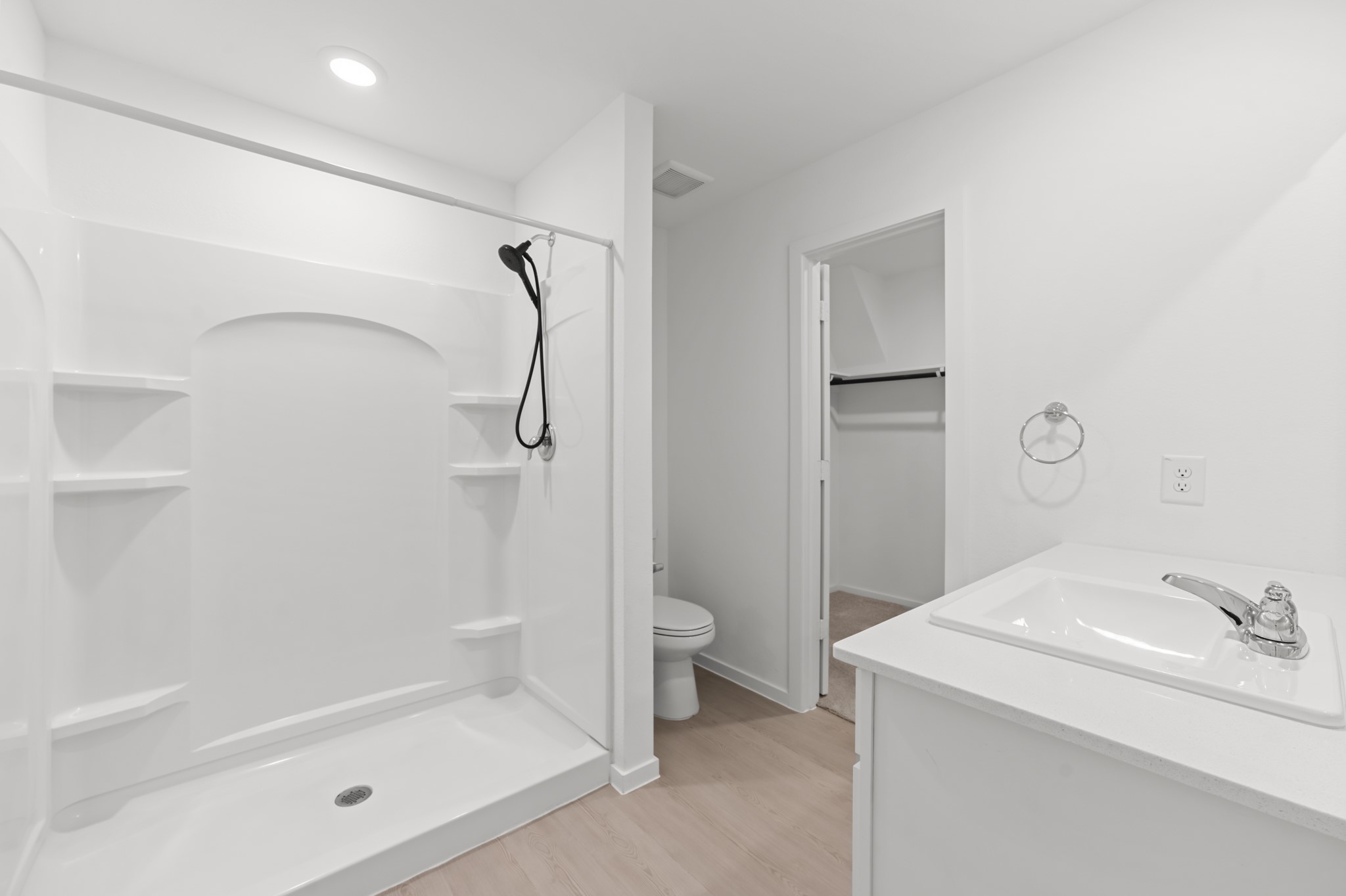 Bright primary bath features a spacious walk-in shower with built-in shelving, a streamlined vanity, and direct access to the walk-in closet.