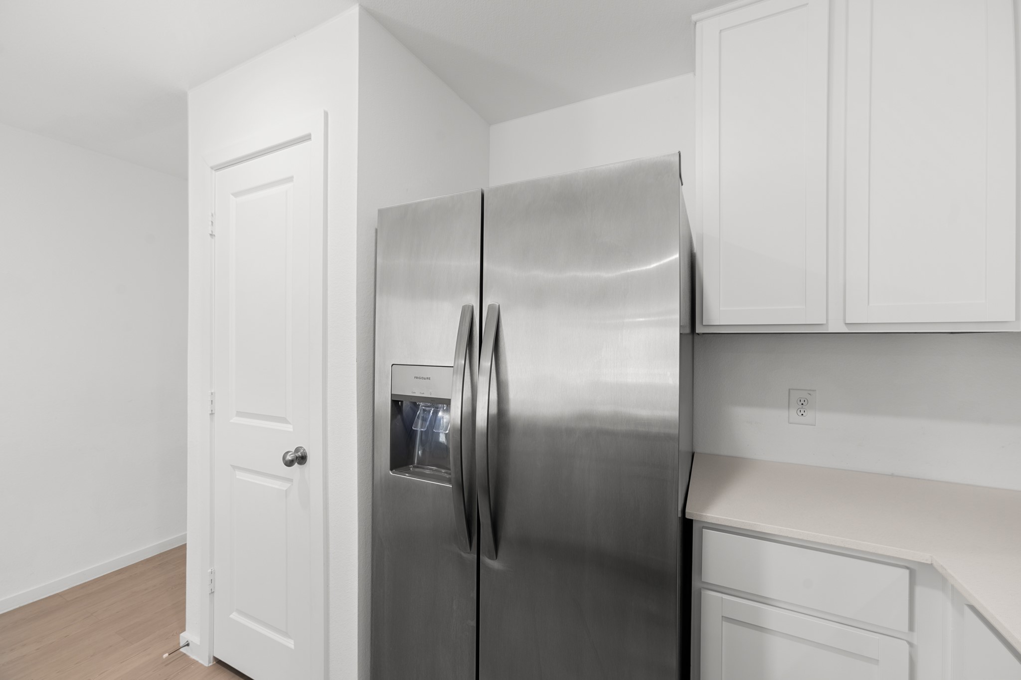 Stainless steel side-by-side refrigerator with in-door water and ice dispenser complements the crisp white cabinetry and adjacent countertop space.