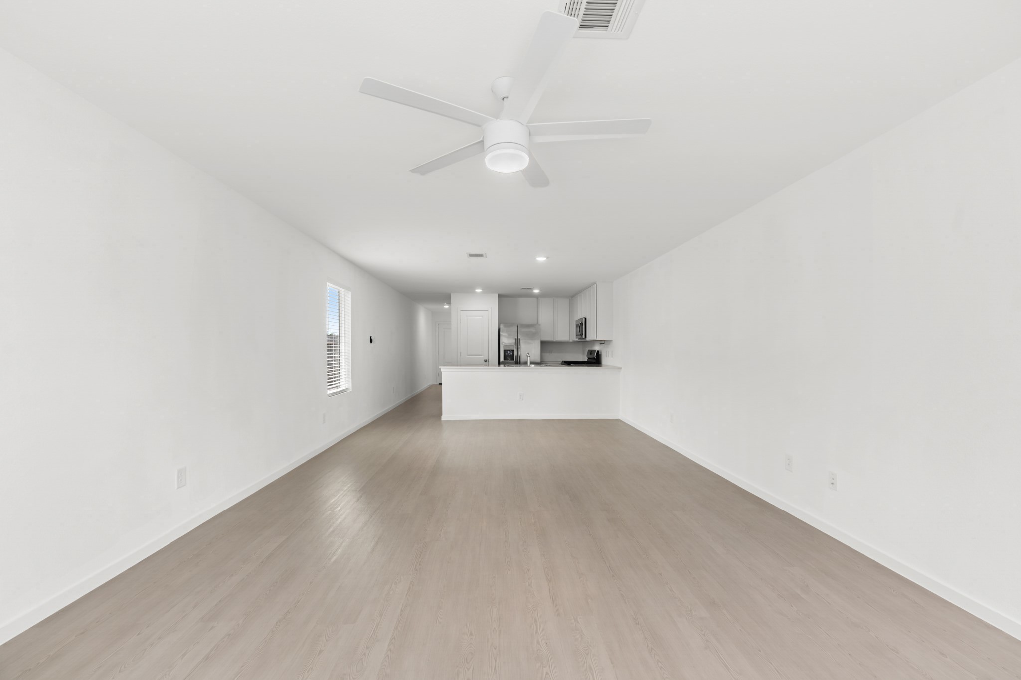 Spacious living room offers a long, open footprint with light-toned flooring, a ceiling fan, and a direct sightline to the kitchen.