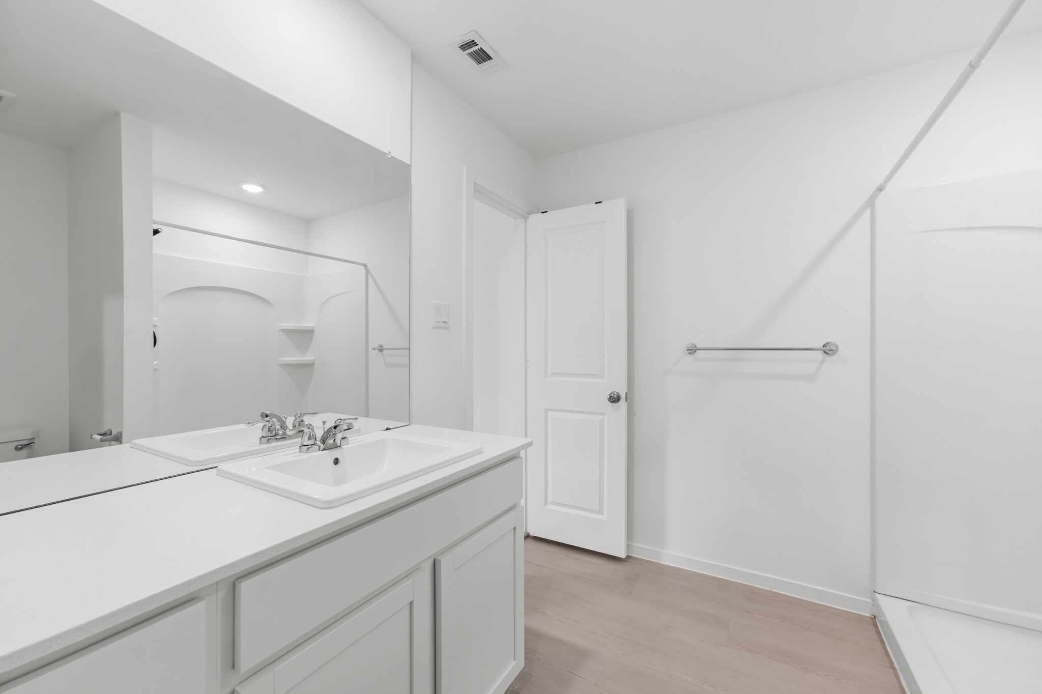Alternate view highlights the generous vanity counter, oversized mirror, neutral finishes, and walk-in shower.