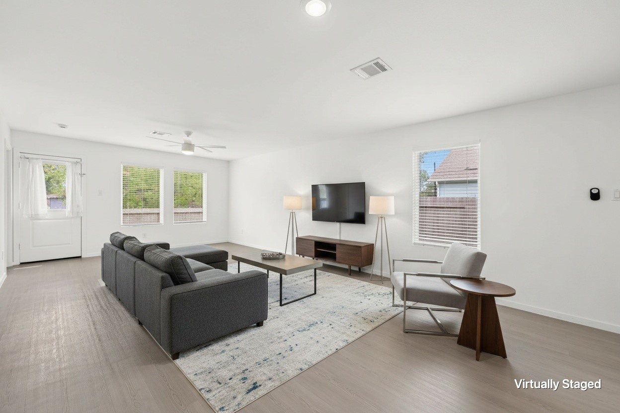 Virtually staged living area highlights the open layout, multiple windows, ceiling fan, and easy connection to the rear entrance.