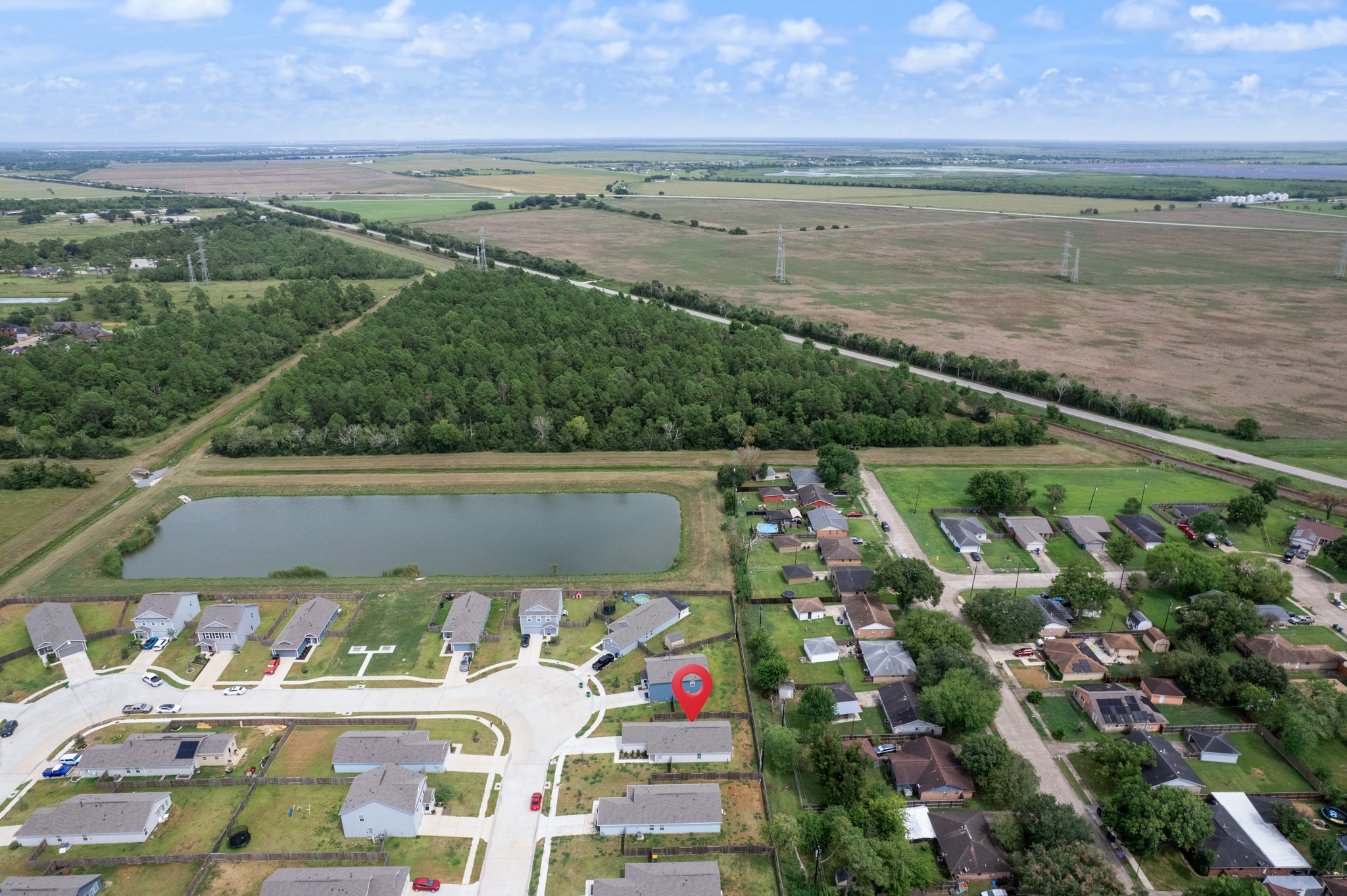 This elevated perspective places the home in context with nearby residential streets, open land, wooded areas, and the community pond.
