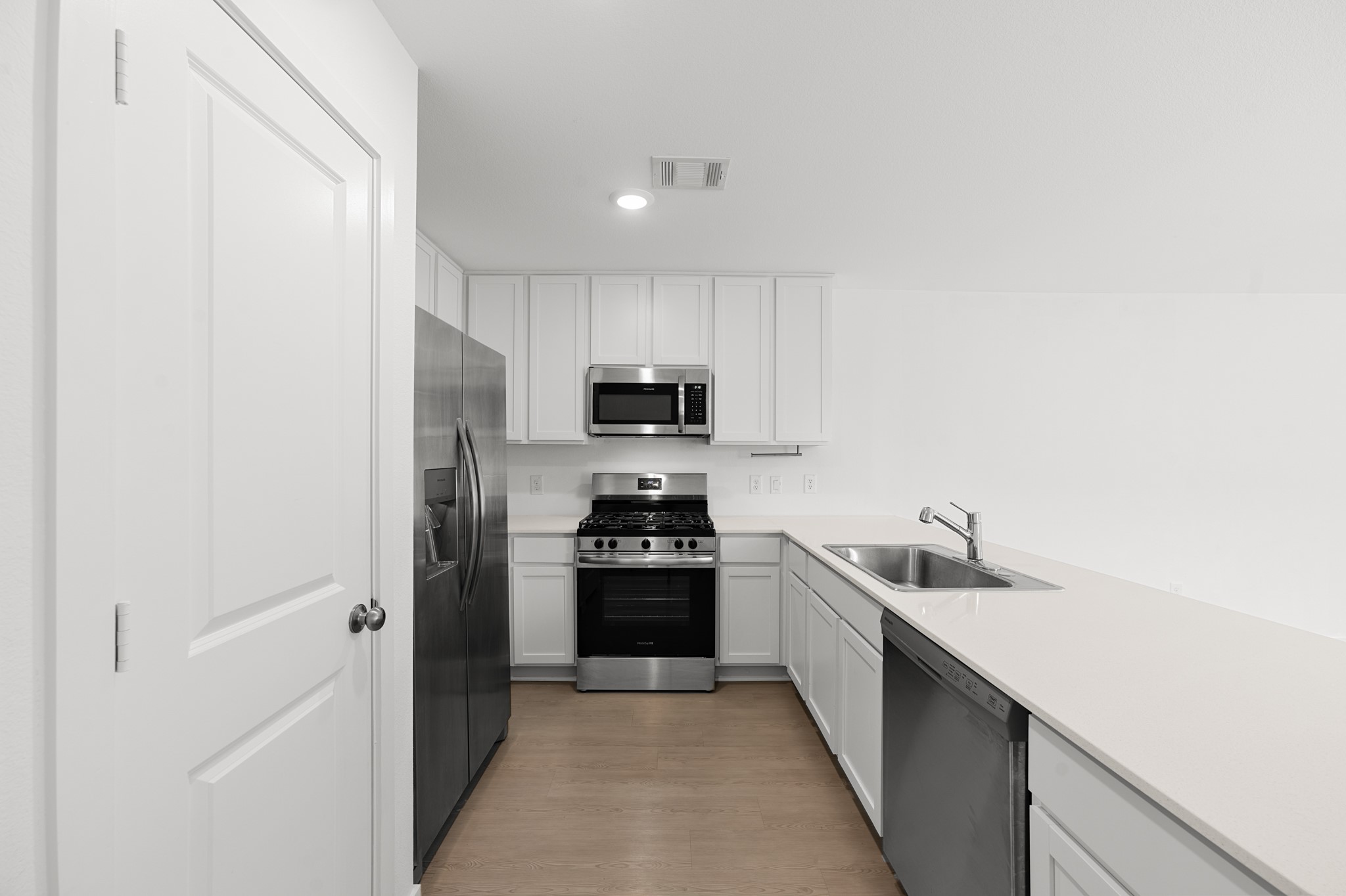 Another view highlights the kitchens efficient layout with white cabinetry, stainless steel appliances, recessed lighting, and ample countertop workspace.