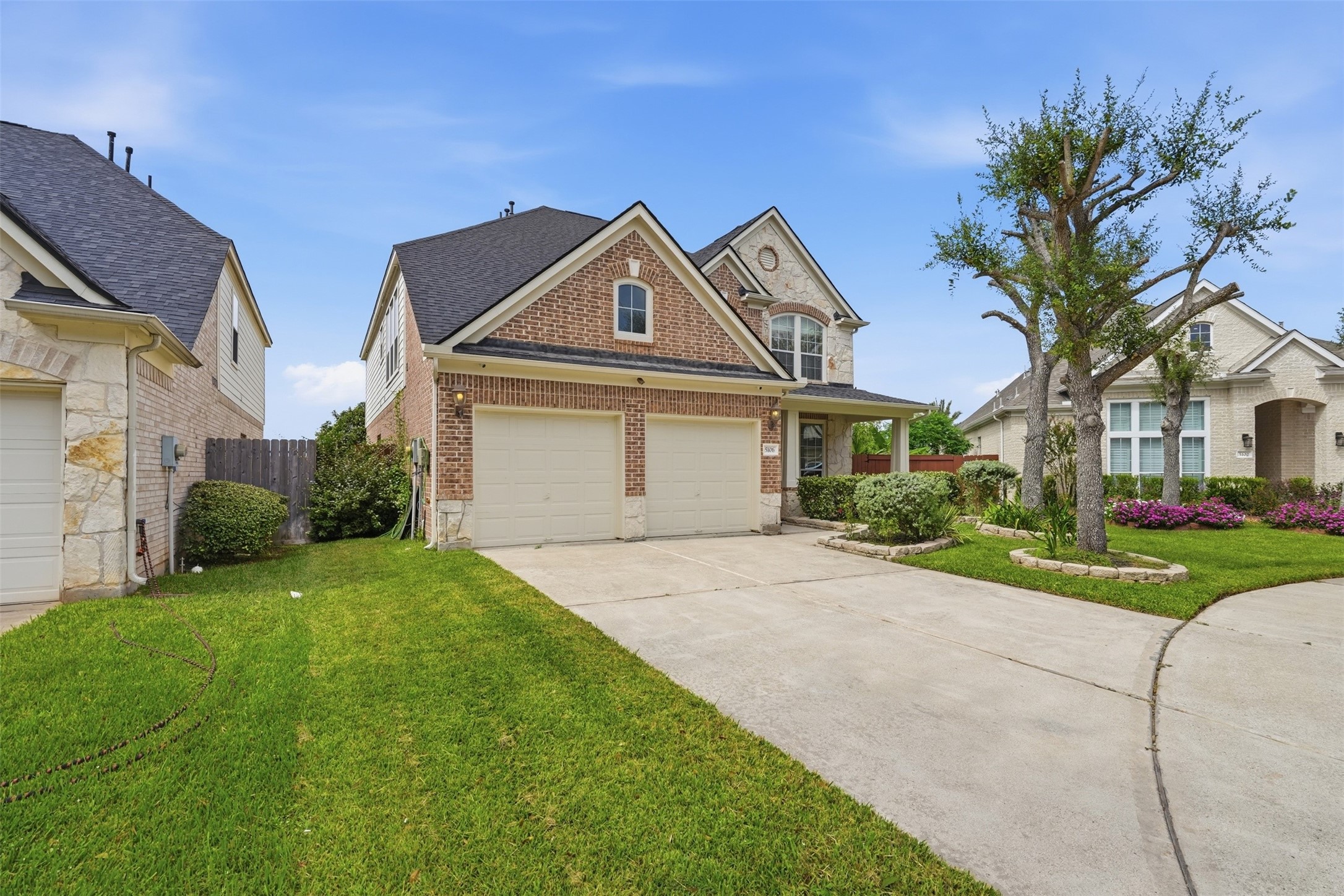 A wide driveway and two-car garage, with a side gate leading to the fully fenced backyard.