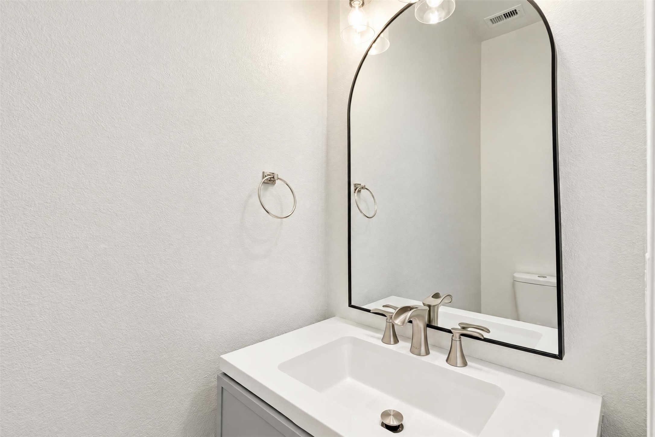 Updated powder room on the main floor for guests, with a modern vanity and an arched mirror.
