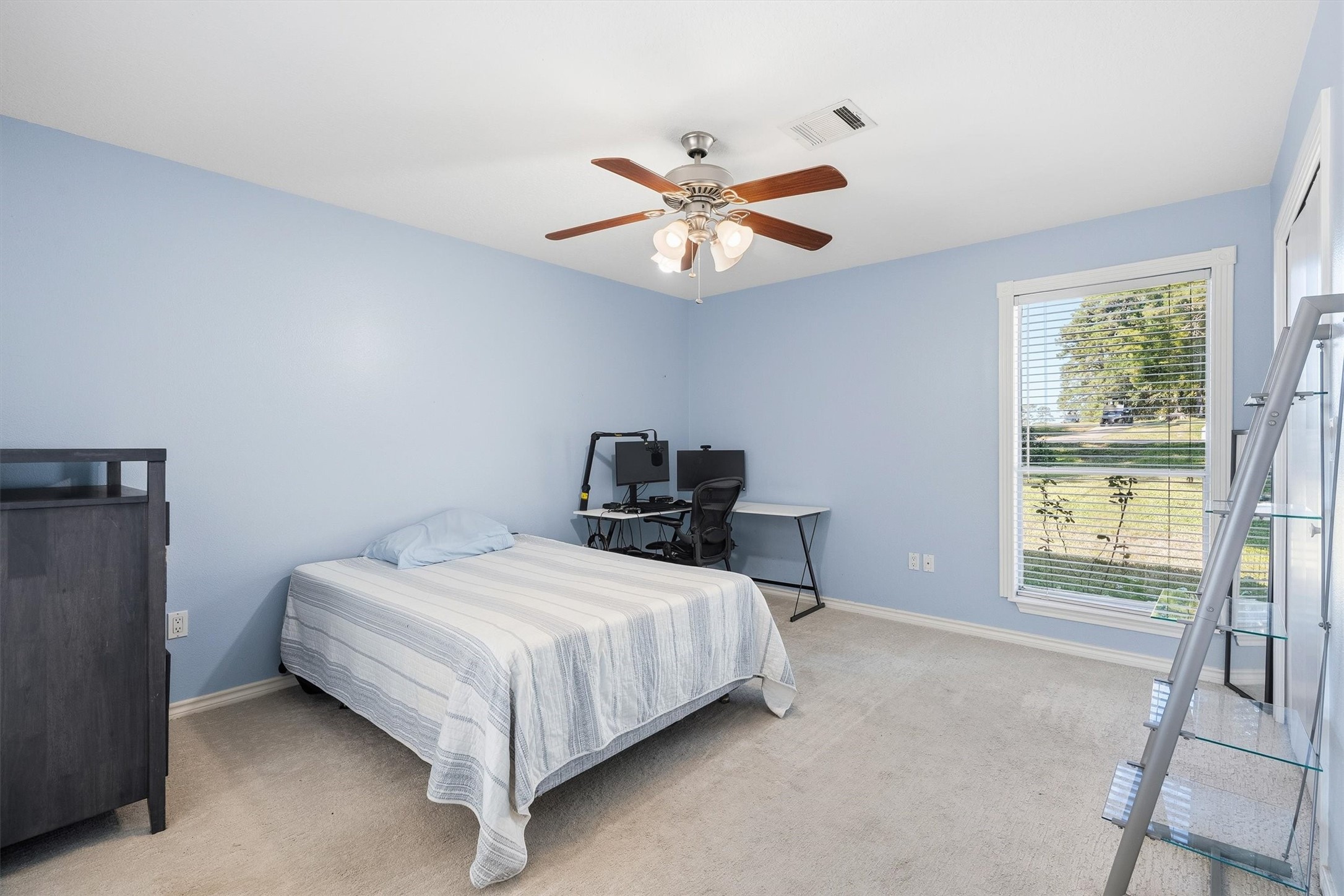 Designed for comfort, this secondary bedroom offers soft carpet, a ceiling fan, and plenty of room for a desk setup alongside the bed.