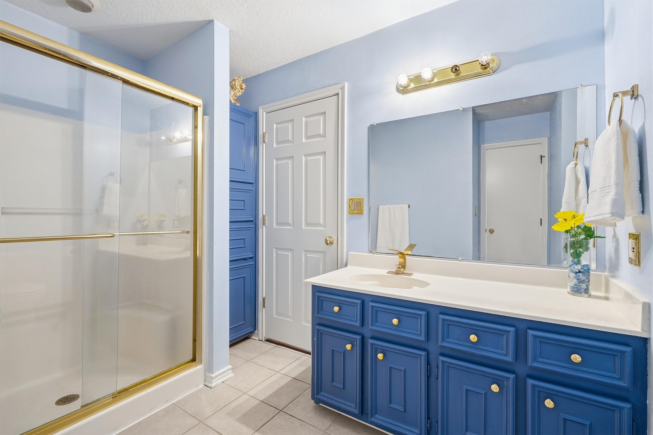 The secondary bath brings a pop of color with navy cabinetry and a built-in linen tower that keeps towels and essentials within easy reach.