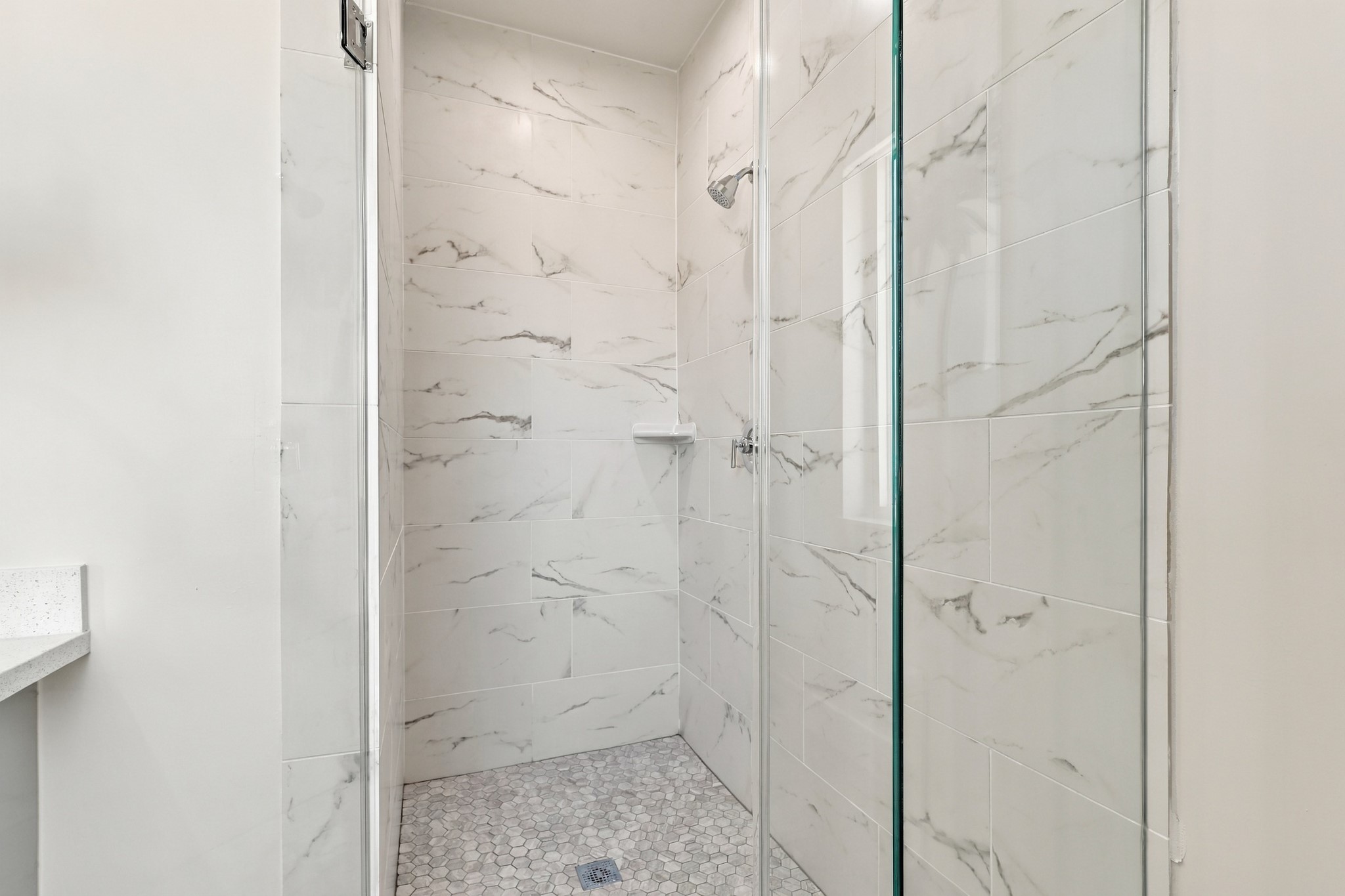 Walk-in shower detail
A glass enclosure showcases the showers elegant marble-look wall tile and mosaic floor. A built-in corner shelf adds convenient storage while maintaining the streamlined design.