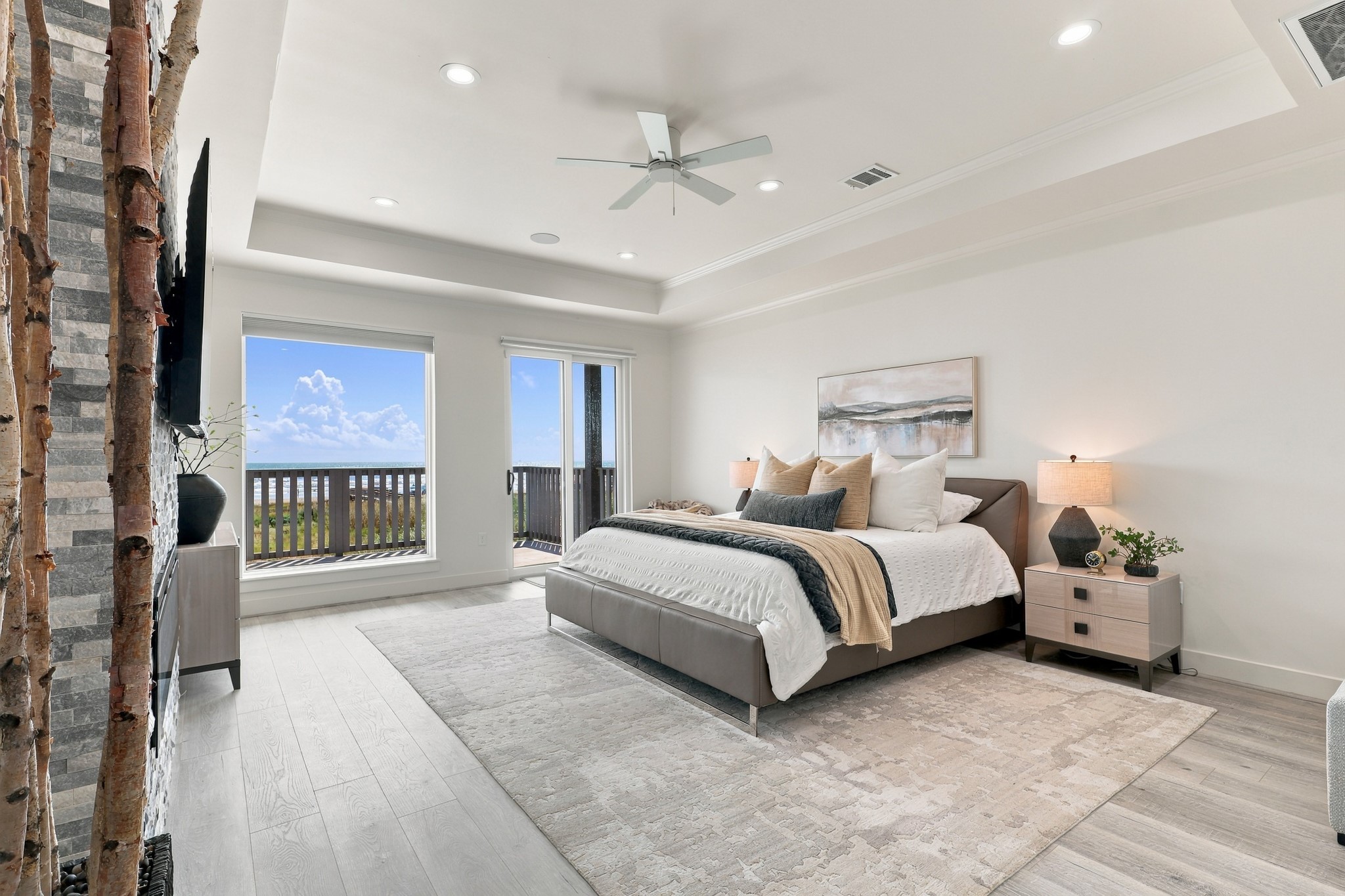 Primary Bedroom- Wake to Gulf views in this spacious bedroom featuring a tray ceiling, recessed lighting, and a textured fireplace accent wall. Sliding glass doors provide direct access to the beachfront deck.