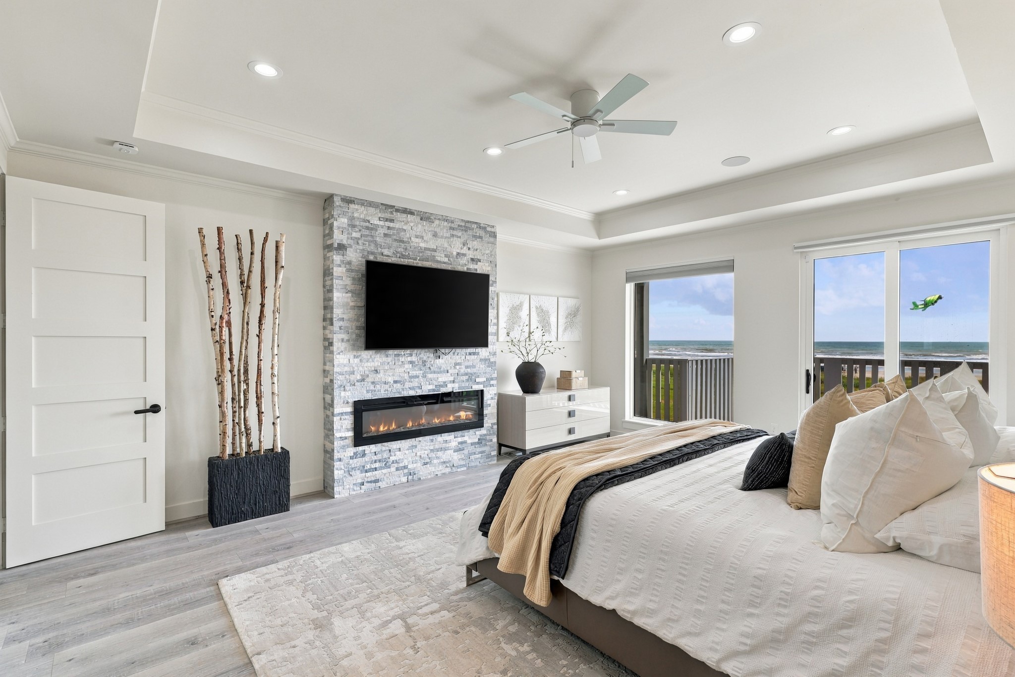 Primary bedroom and fireplace
The primary retreat features a stacked-stone fireplace wall, an architectural tray ceiling, and direct access to the beachfront deck. Generous windows bring Gulf views into this inviting space.
