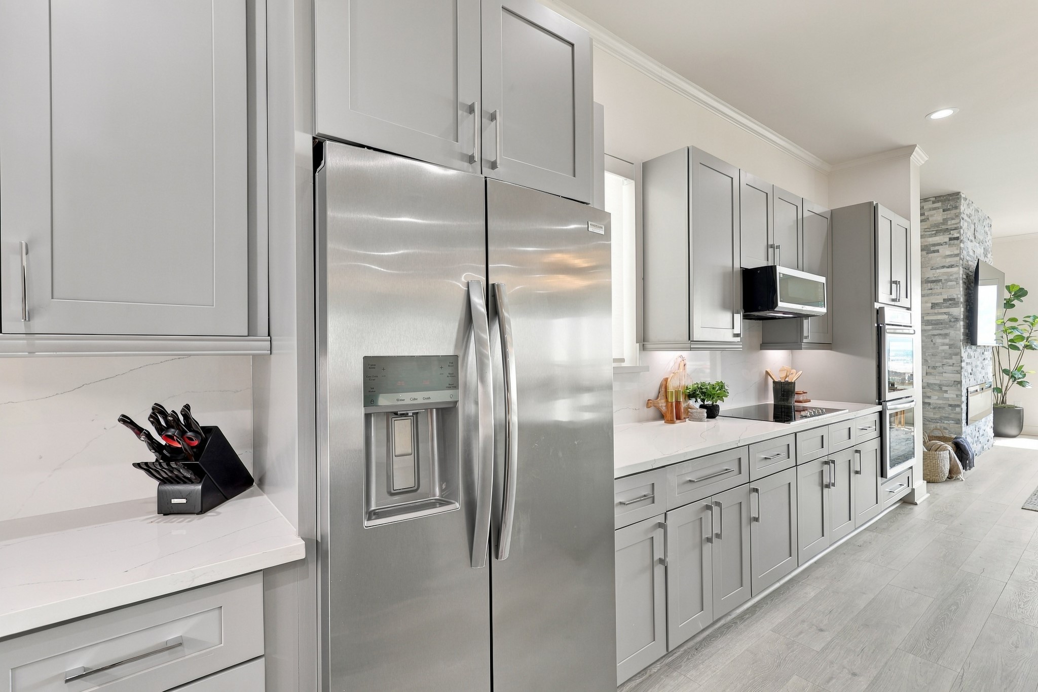 Stainless steel appliances pair with gray cabinetry and a coordinating backsplash for a cohesive, contemporary finish. Under-cabinet lighting illuminates the extended preparation area.