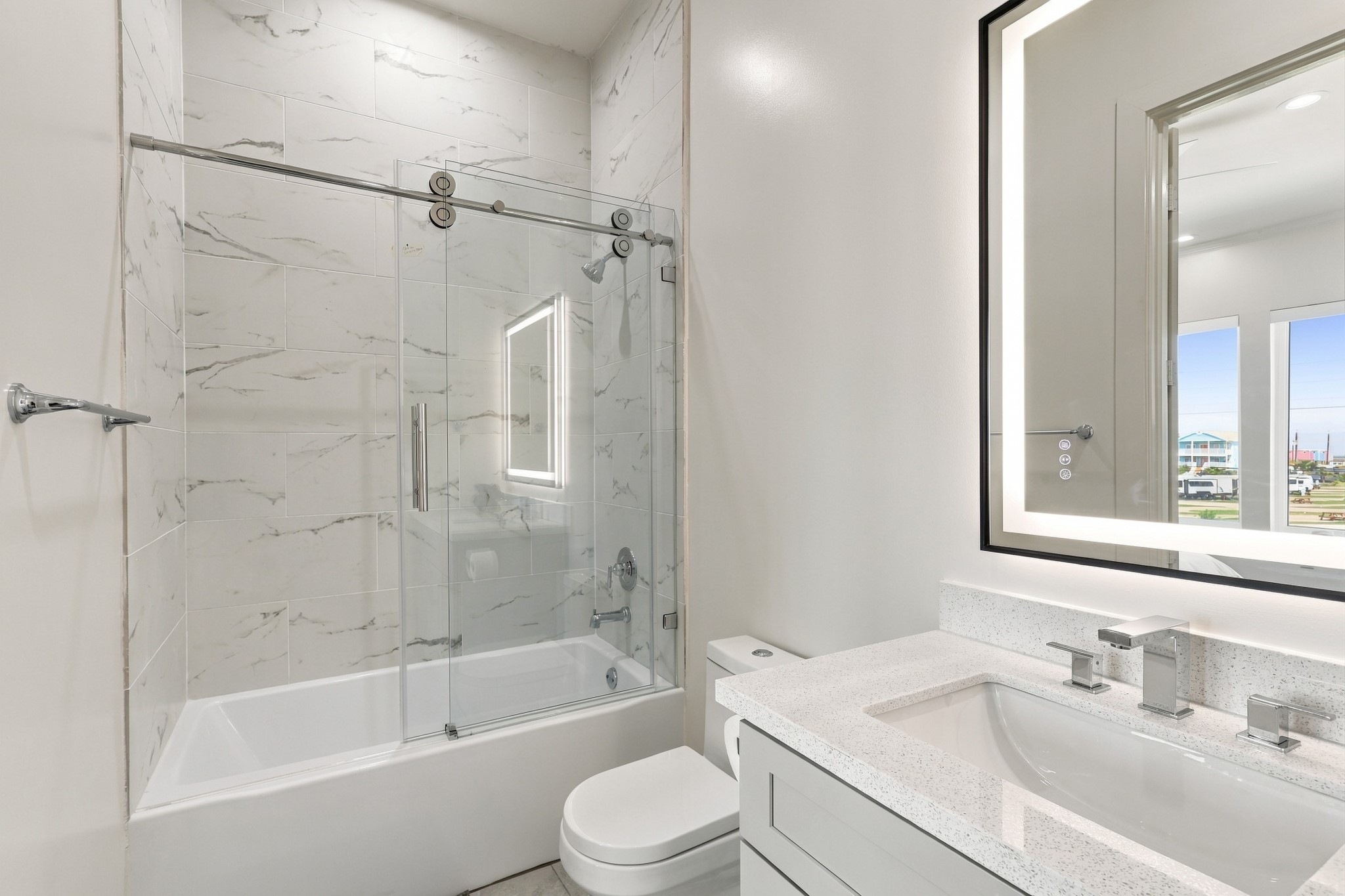 Full bathroom
Contemporary bathroom featuring a tub-and-shower combination with sliding glass doors and marble-look tile extending to the ceiling. An illuminated mirror and streamlined vanity complete the space.