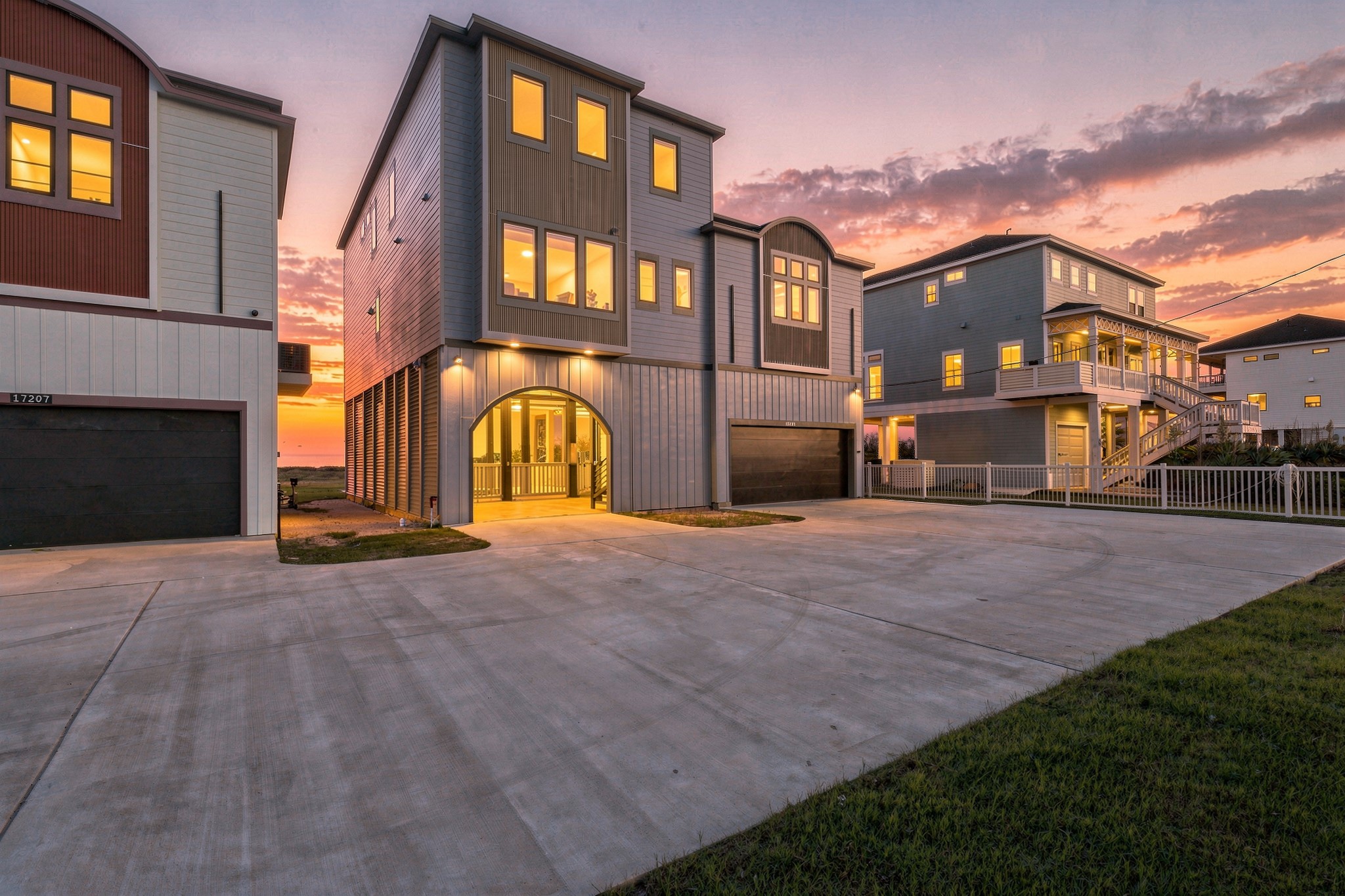 Contemporary beachfront retreat with striking architectural lines, an illuminated covered entry, and a spacious driveway. Warm evening lighting creates an inviting arrival.