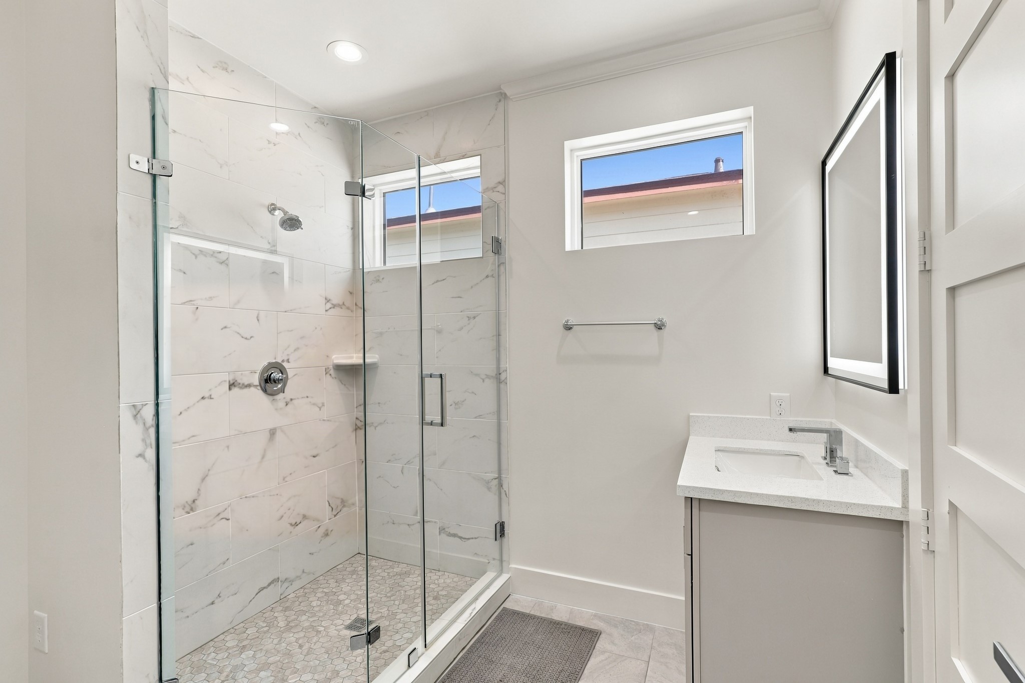 Full bathroom, alternate view
Natural light enters through high windows in this thoughtfully finished bathroom. A glass-enclosed shower with marble-look tile, mosaic flooring, and a coordinating vanity creates a cohesive coastal look.
