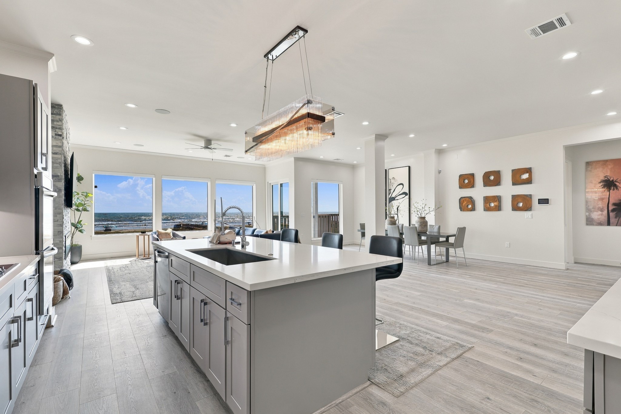 The generous kitchen island offers ample preparation space and casual seating, with views extending through the living area to the Gulf beyond.