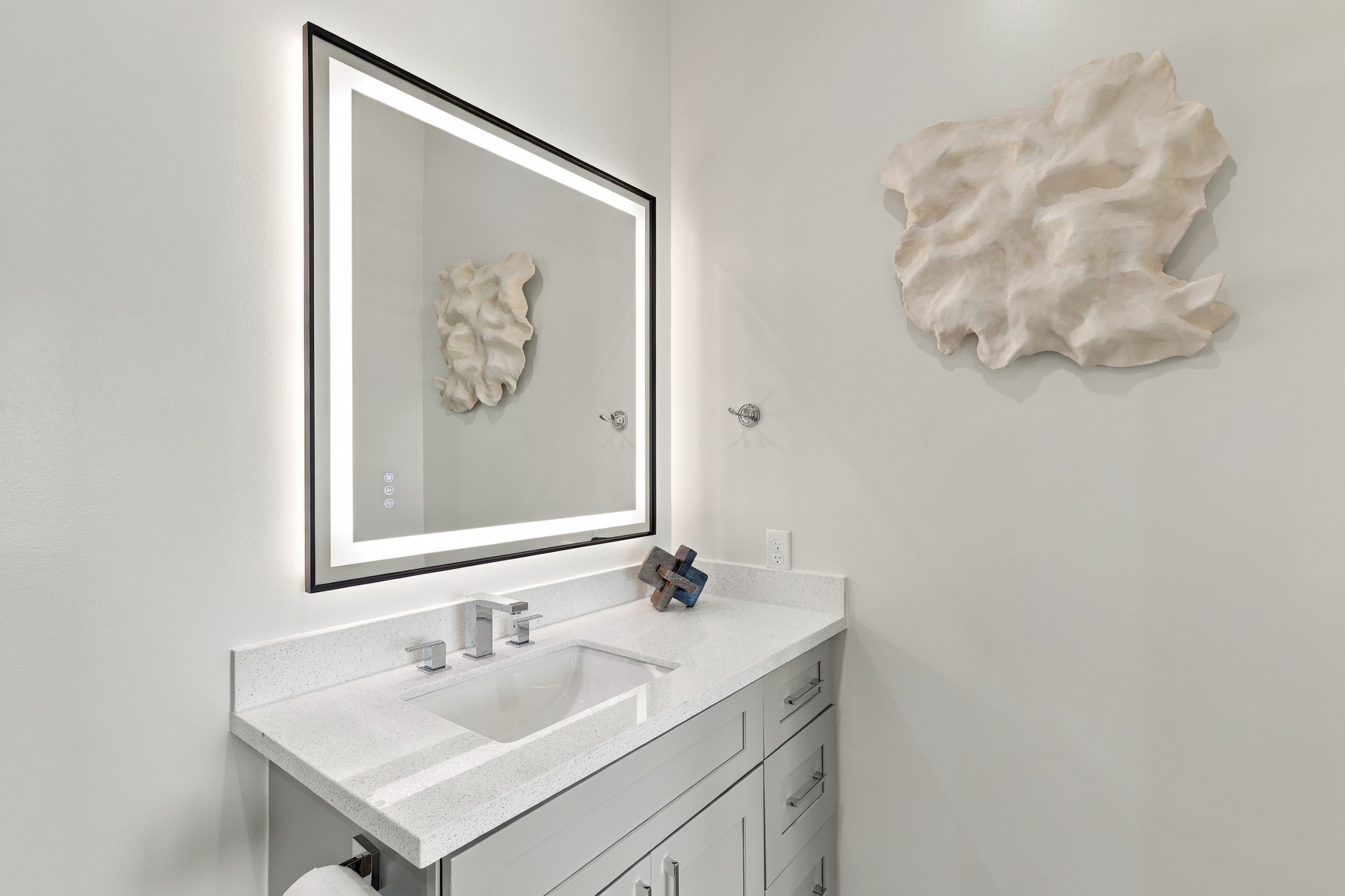 Bathroom vanity detail
A softly illuminated mirror and chrome fixtures complement the light countertop and gray cabinetry. Generous vanity storage keeps the space both practical and refined.