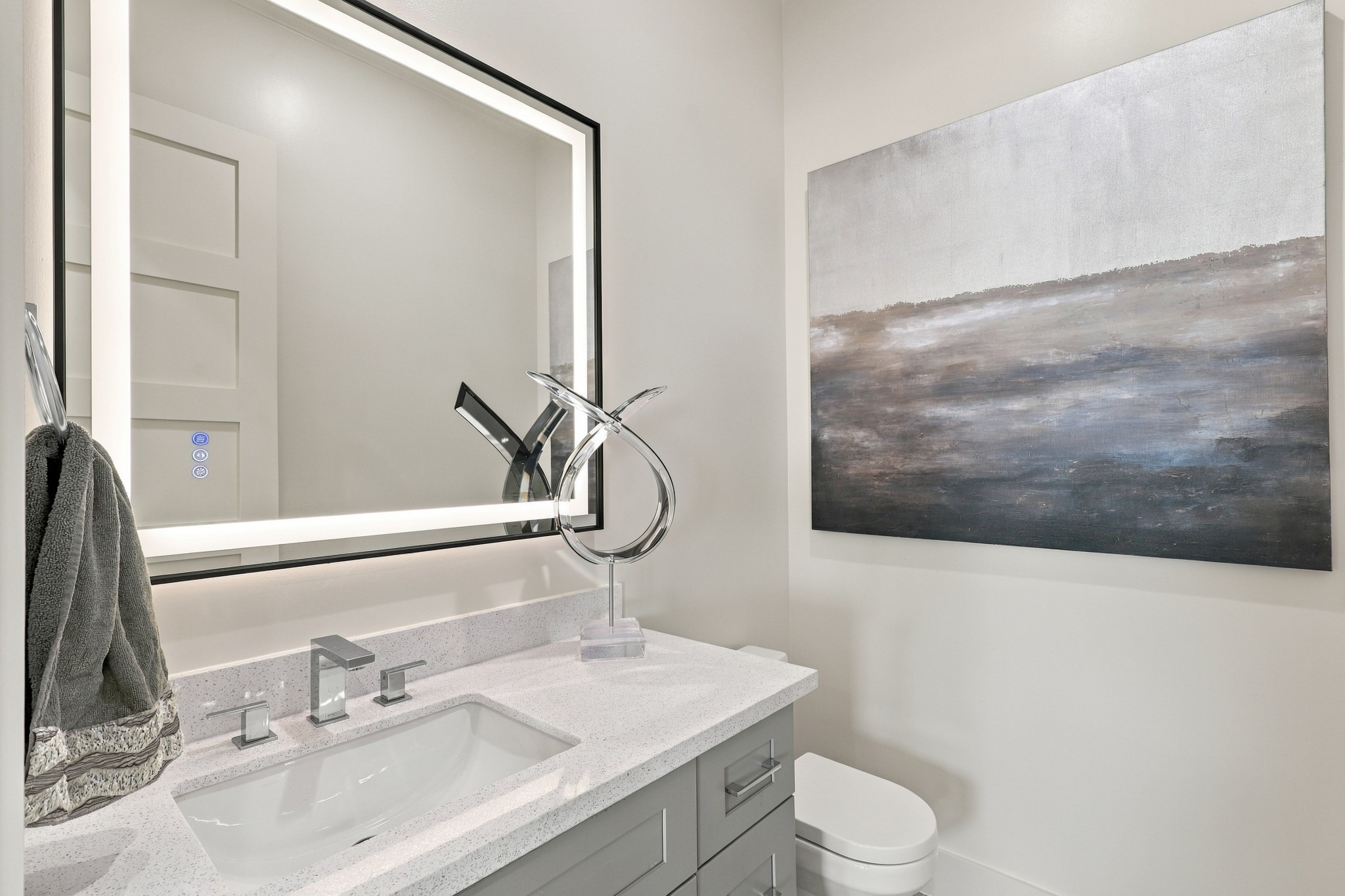 Stylish powder room/ Half Bath with a light countertop, gray vanity, contemporary chrome fixtures, and an illuminated mirror. Clean lines carry the homes modern aesthetic into this thoughtfully finished space.