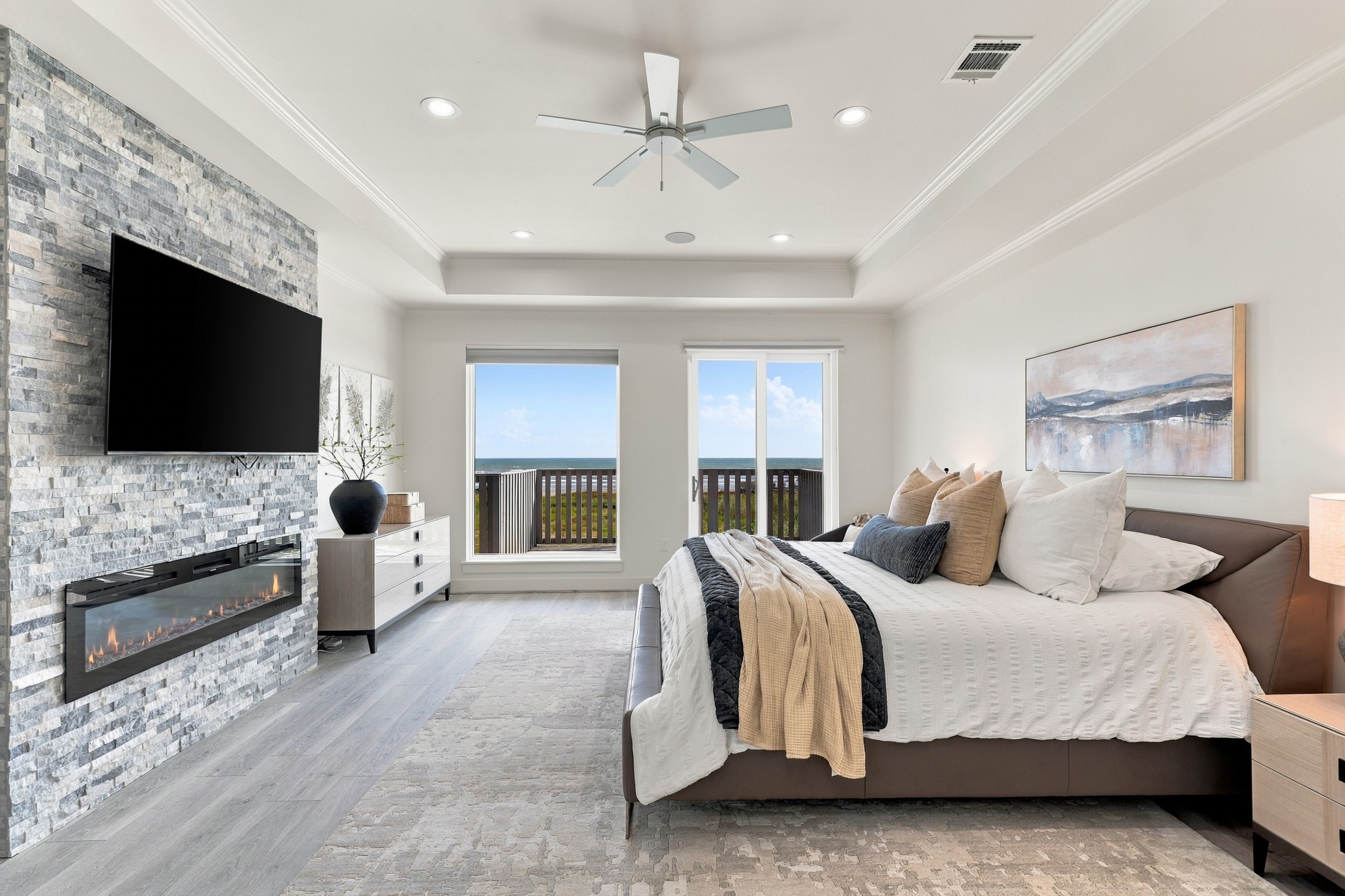 Primary bedroom, alternate view
This alternate perspective highlights the primary bedrooms spacious proportions and elegant coastal finishes. A linear fireplace and deck access create a comfortable setting for quiet evenings by the water.