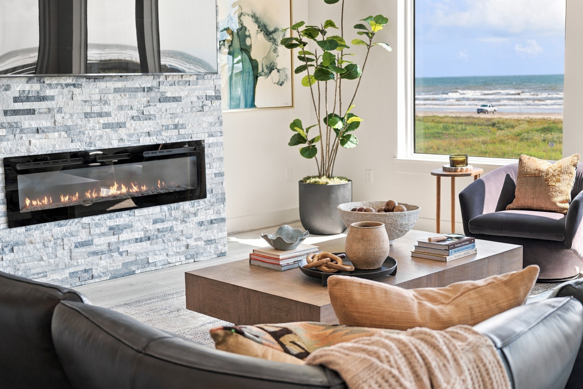 Fireplace detail
A sleek linear fireplace set within a textured stacked-stone surround creates a striking living-room focal point. The adjacent window frames the shoreline, pairing coastal scenery with an inviting interior.
