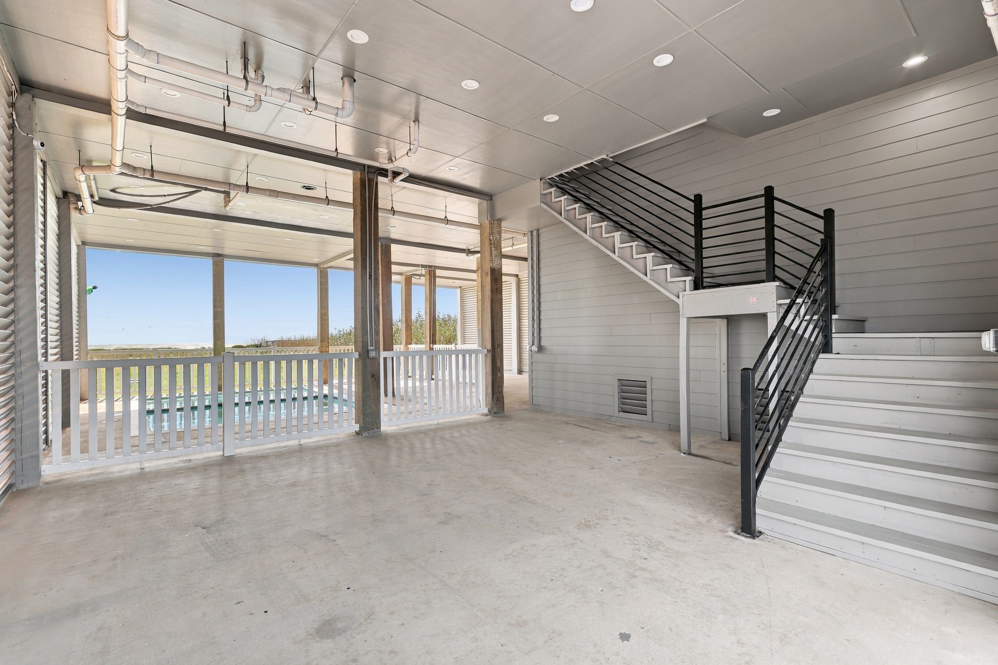 Covered ground-level space
Expansive covered ground-level space offers room for outdoor seating and gathering beside the pool area. Recessed lighting and an interior staircase connect this sheltered setting to the home above.