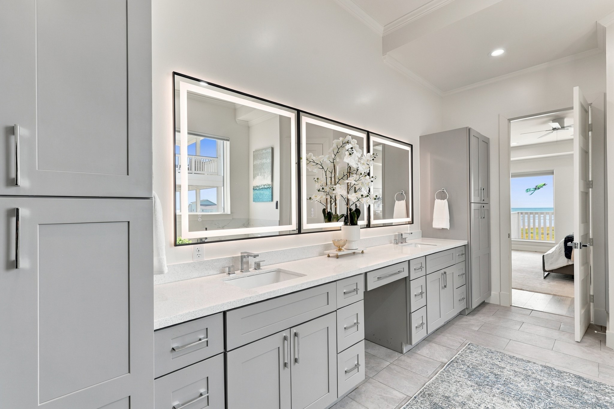 Primary vanity
The extended dual-sink vanity offers abundant drawer storage, tall cabinets, and a dedicated seated preparation area. Three illuminated mirrors brighten the space and complement its contemporary finishes.