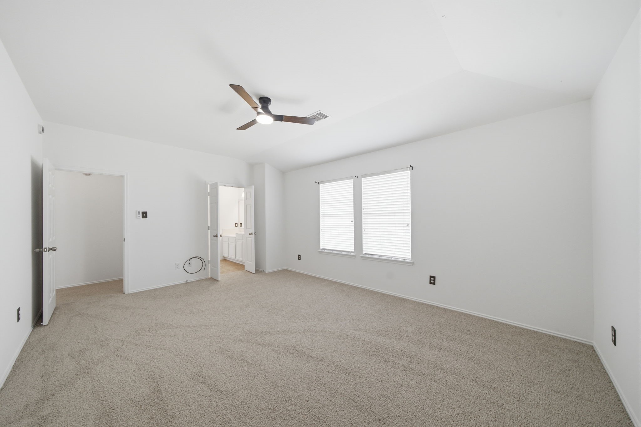 Soft neutral carpet and a vaulted ceiling with a modern fan define this light-filled secondary bedroom. Crisp white walls and dual windows create an open, airy atmosphere with plenty of space for personalized furnishings.