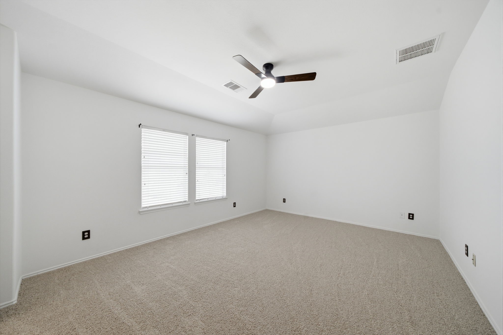 Neutral carpet flooring, a tray ceiling, and a modern ceiling fan anchor this bright secondary bedroom. Dual windows fill the space with natural light, offering a versatile layout for guest accommodations or a home office.