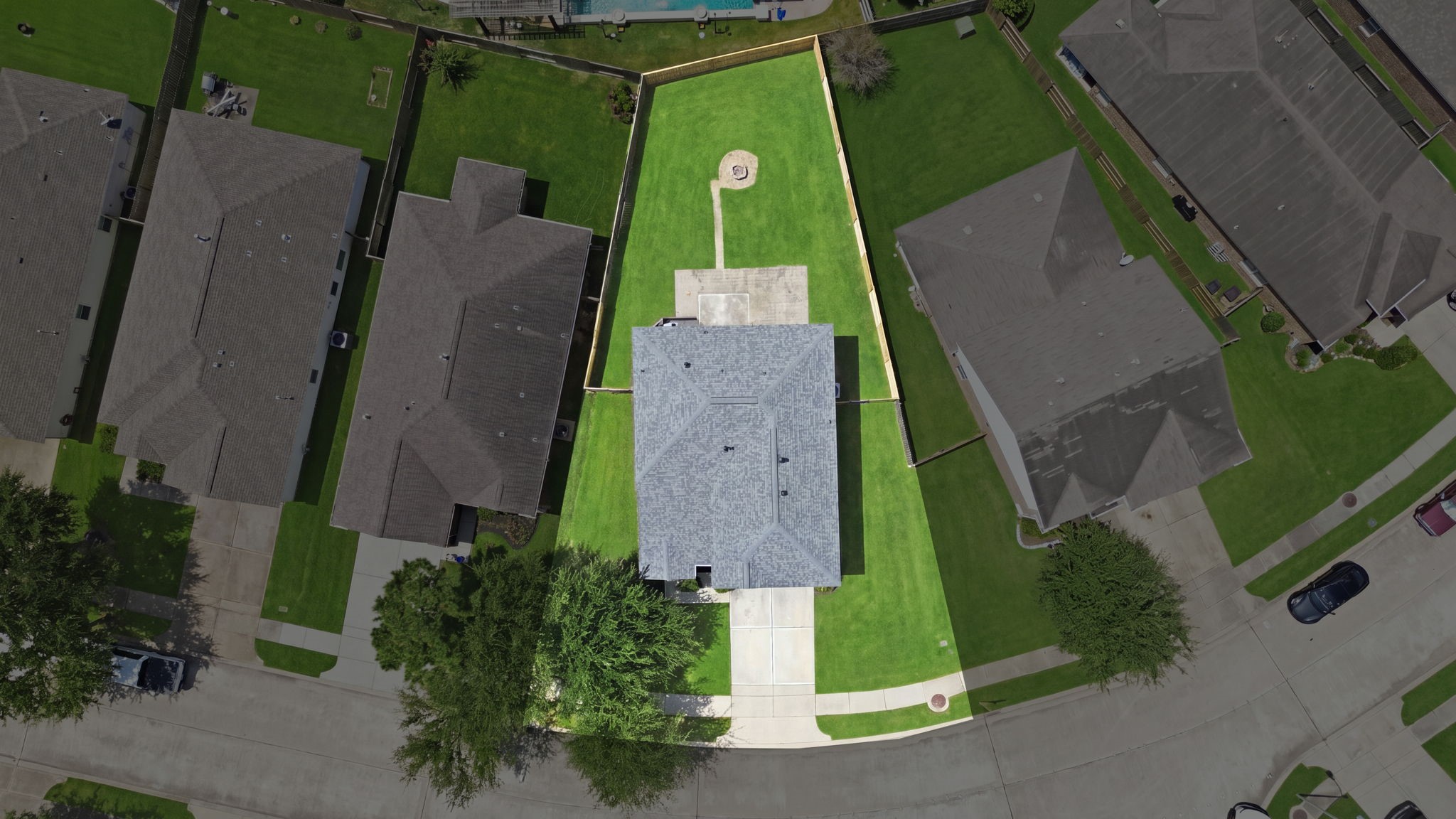 Aerial view reveals the deep lot shape, highlighting the sprawling backyard space with its central fire pit and patio setup.