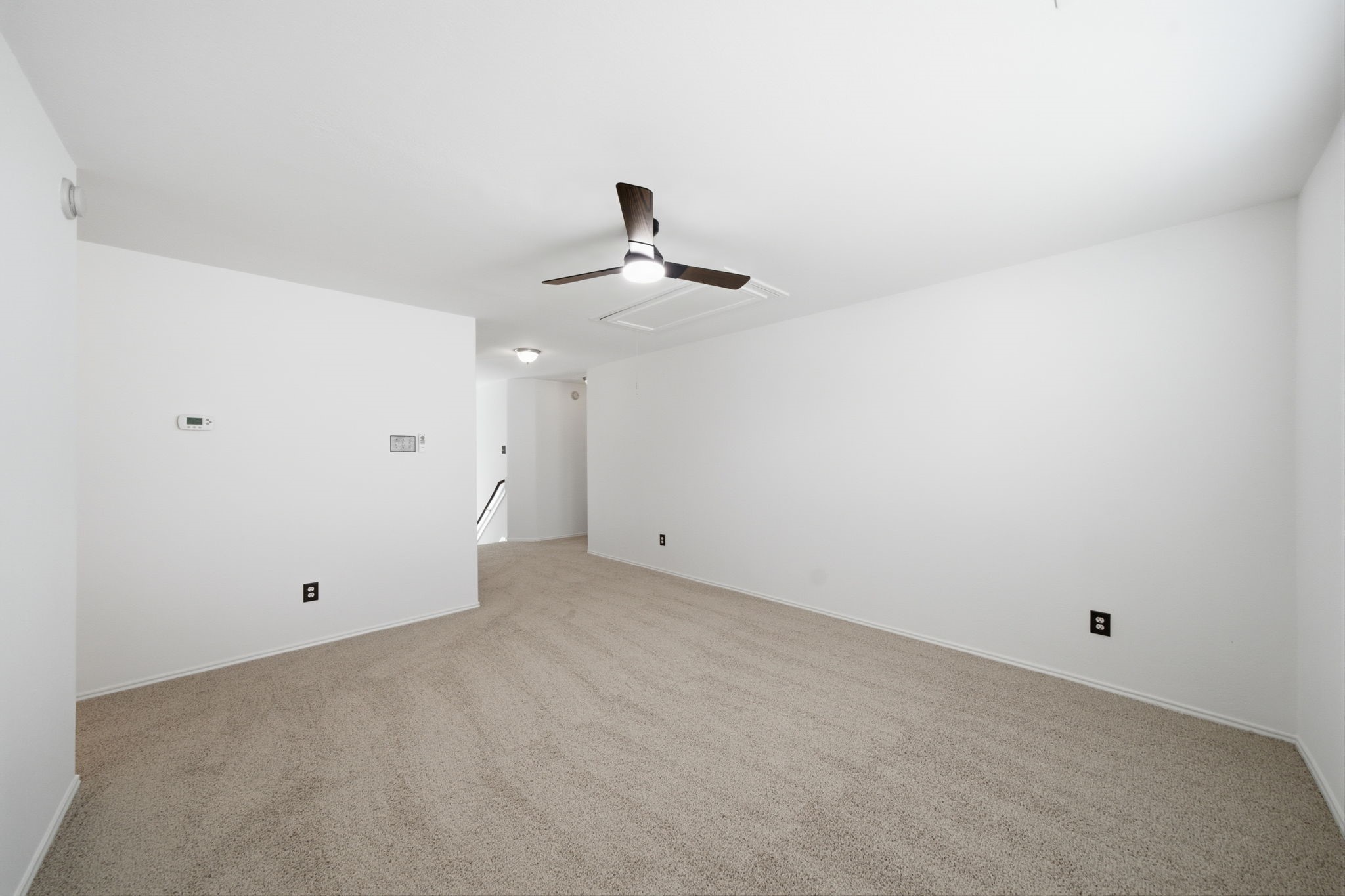Soft carpet flooring and fresh neutral paint frame this flexible second-floor gameroom with a central ceiling fan. An open layout connects directly to the hallway, offering a versatile space for recreation or lounging.