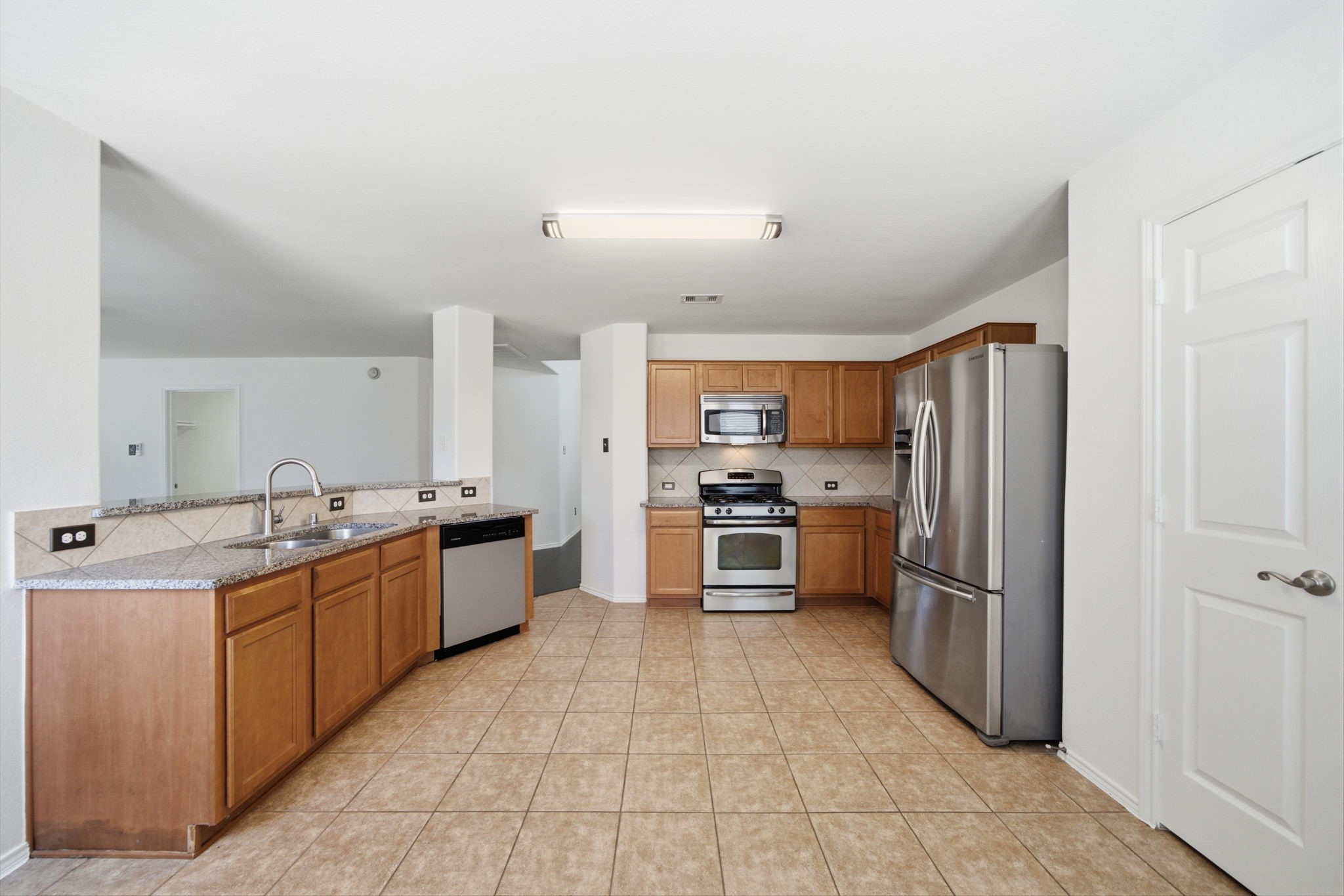 Spacious and functional, this updated kitchen features warm wood cabinetry, granite countertops, and stainless steel appliances. Tile flooring runs throughout, while a raised breakfast bar offers continuous sightlines into the main living areas.