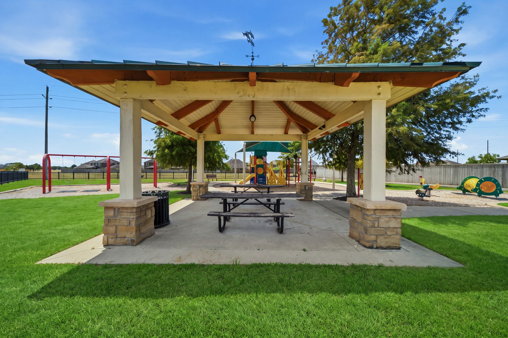 Shaded by a spacious pavilion with stone-accented pillars and picnic tables, this park area sits adjacent to a vibrant neighborhood playground.