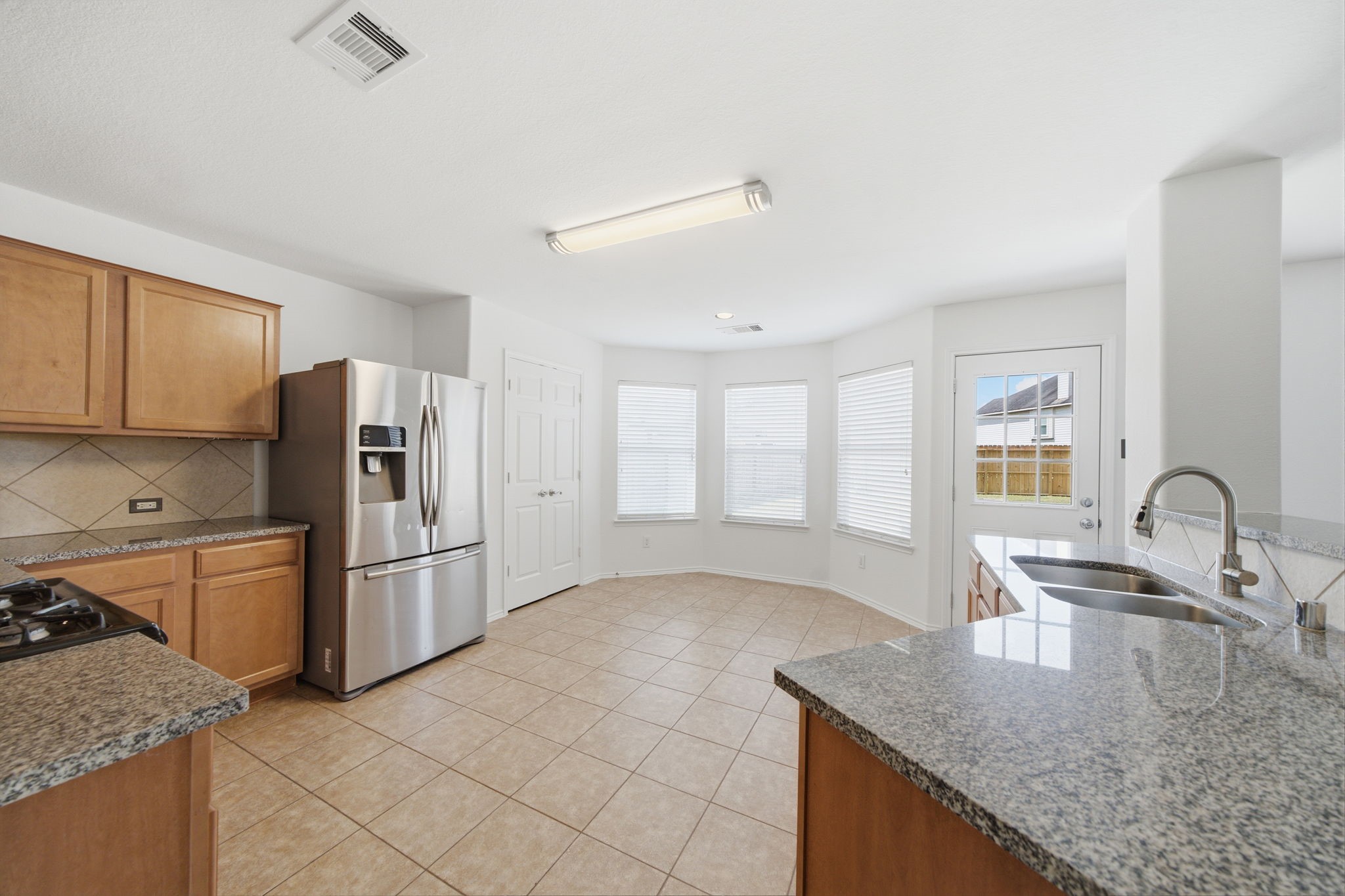 Warm wood cabinetry and granite countertops frame this updated kitchen, complete with a gas cooktop and stainless steel appliances. A raised breakfast bar overlooks the main living space, while tile flooring leads directly into the sunlit breakfast nook.