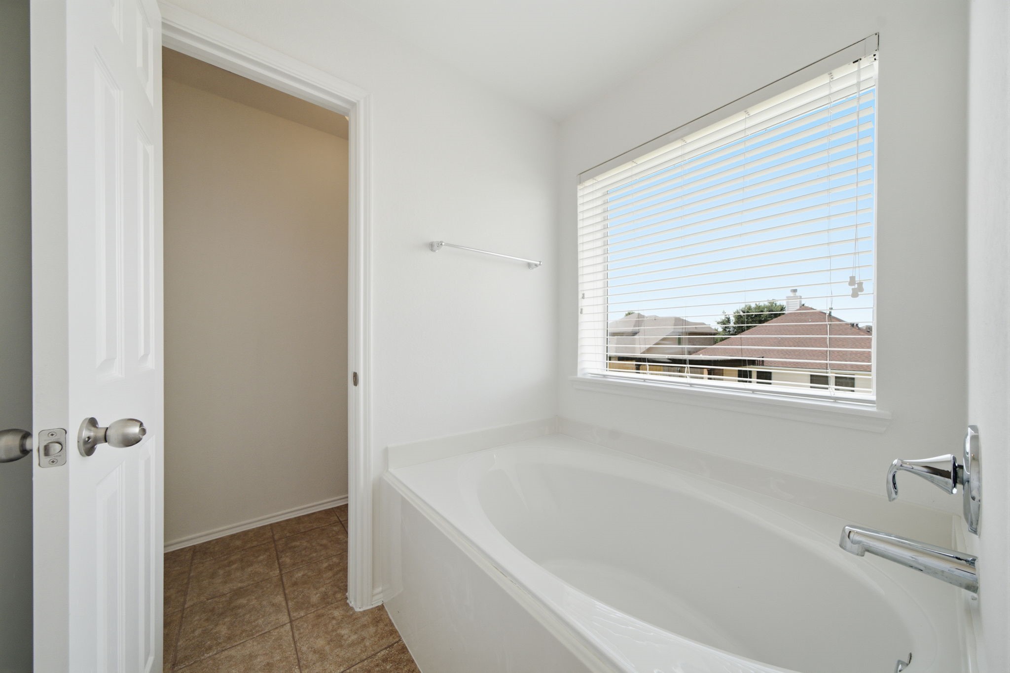 A deep oval soaking tub sits beneath a wide window, serving as the focal point of this primary bath. Tile flooring and a crisp white finish create a light-filled setting designed for relaxation.