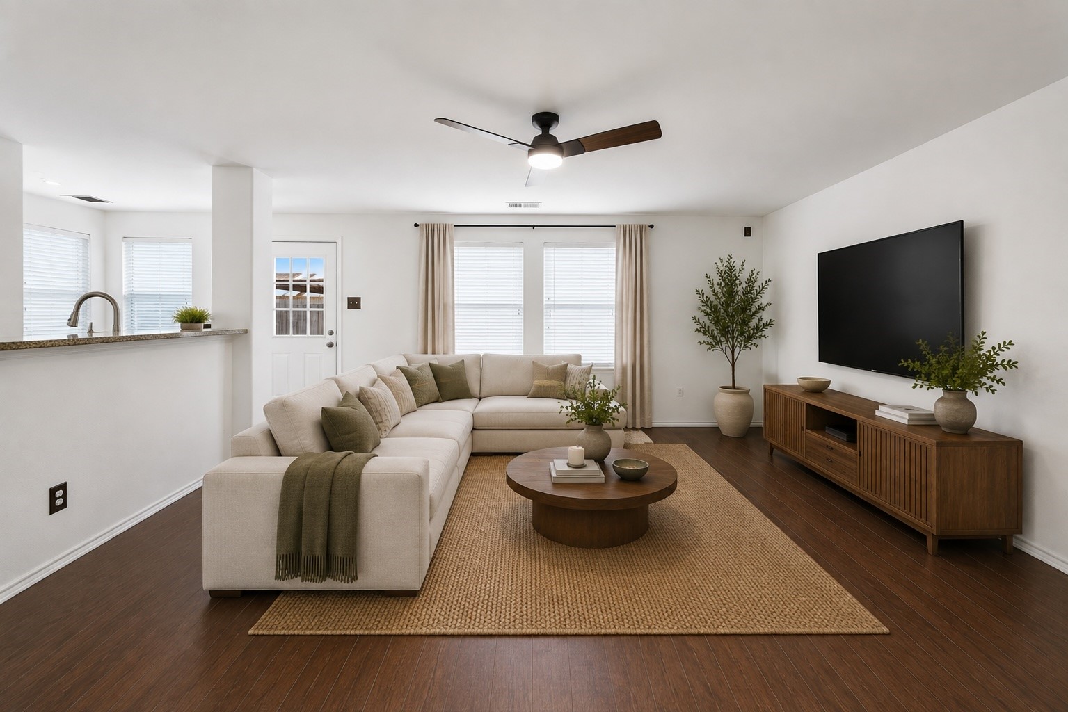 An open-concept living area boasts rich wood-look floors, a ceiling fan, and seamless sightlines into the adjacent kitchen via a raised breakfast bar. Crisp neutral walls and large windows offer a bright, functional space designed for everyday relaxation and entertaining. This photo has been virtually staged.