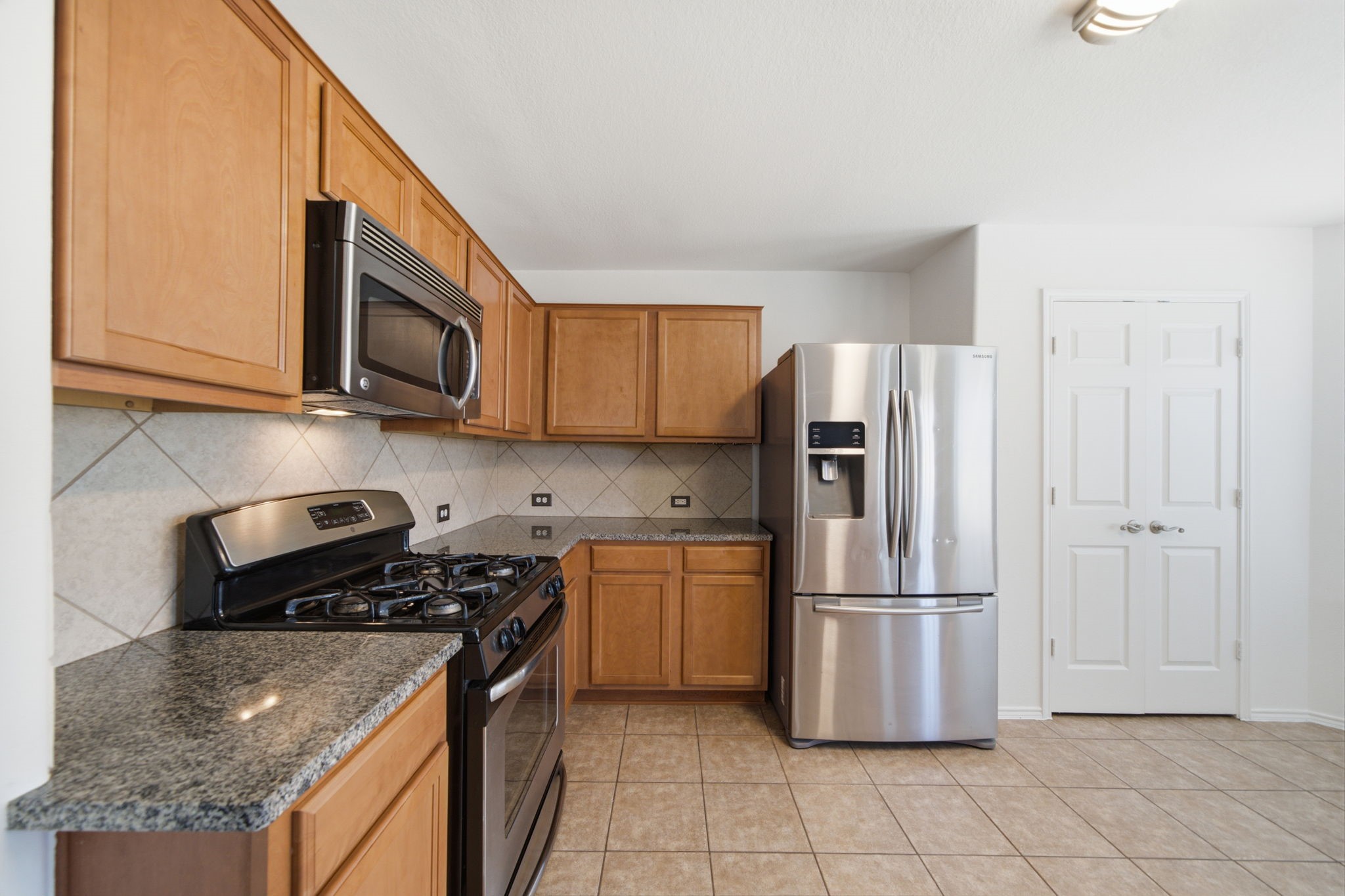 Stainless steel appliances and rich granite countertops highlight this updated kitchen, outfitted with a gas cooktop and an over-the-range microwave. Warm wood cabinets and a tile backsplash offer plentiful storage and functional workspace.